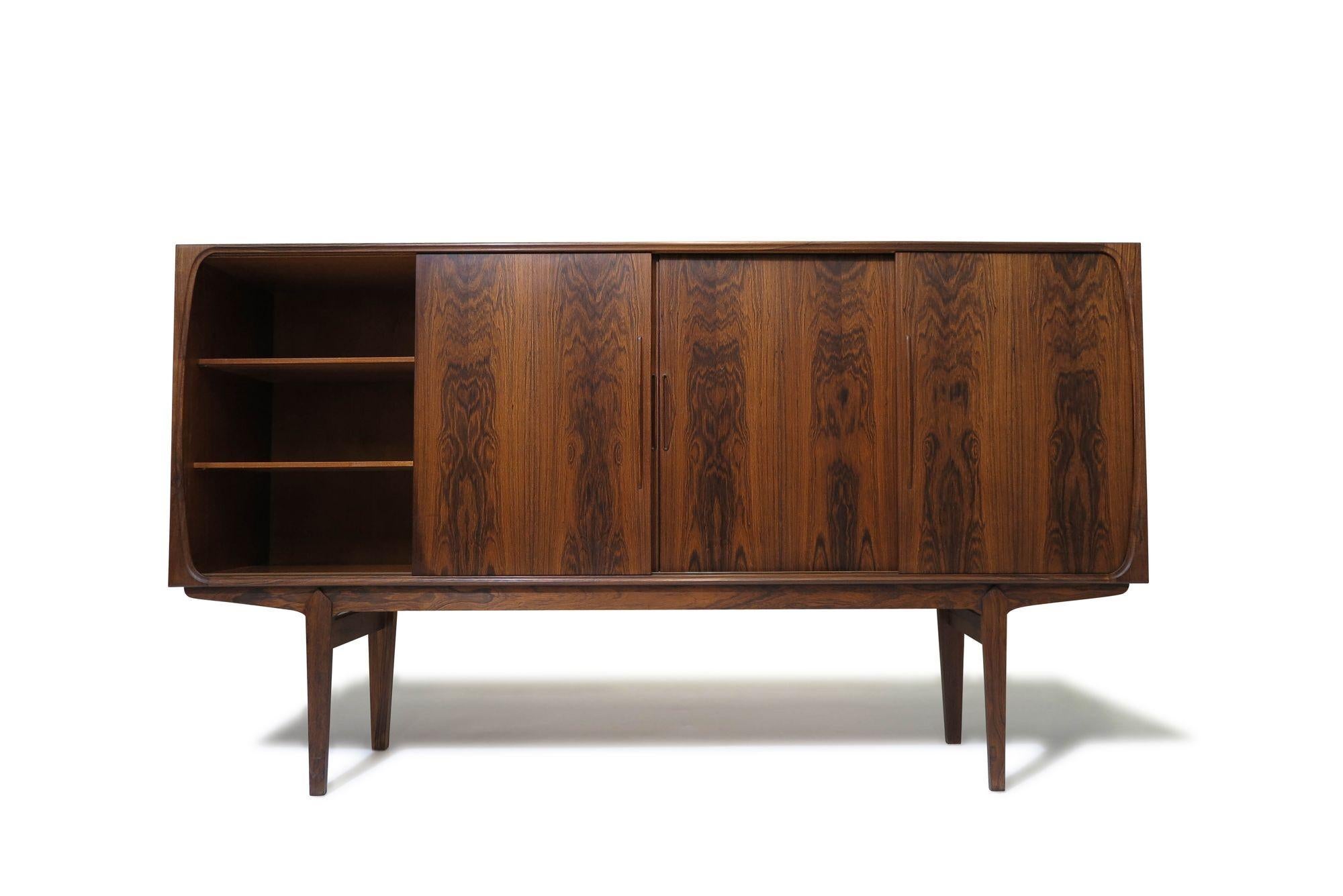 Mid-century Danish Brazilian Rosewood sideboard credenza with stunning book-matched grain, raised on stilted legs. The cabinet features four sliding doors with sculpted pulls, revealing a mahogany interior with adjustable shelves, and a center