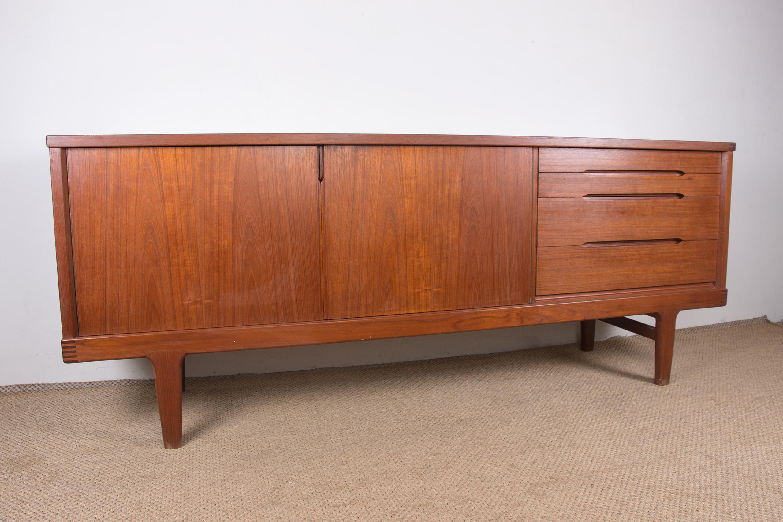 Beautiful Scandinavian sideboard in an elegant Brutalist style. Two sliding doors on the left open to reveal a large shelf. Four drawers of varying sizes on the right, each with integrated handles. The back is teak veneered, offering visibility from