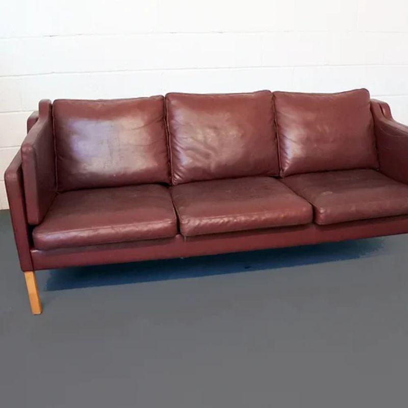 A Danish burgundy leather upholstered three seater sofa with pale wood legs and complete with seat and back cushions as well as unusual double arm cushions, attributed to Borge Mogensen, 1960s.

Additional Information:
Material: Leather,