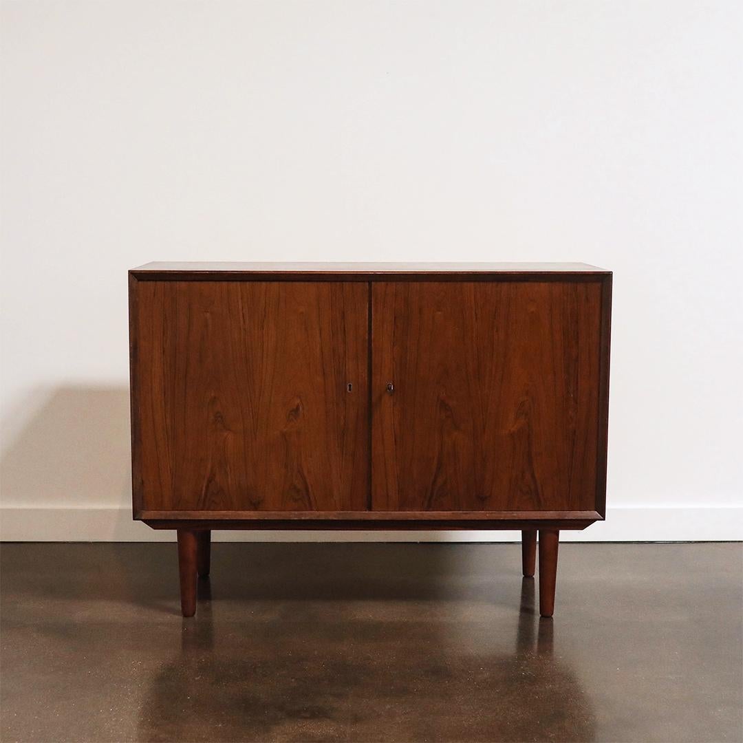 Mueble moderno de mediados de siglo, de palisandro, con líneas limpias, puertas a juego y patas sutilmente ahusadas. Incluye una cerradura que funciona con llave original, estanterías ajustables y un veteado bellamente figurado que resalta la