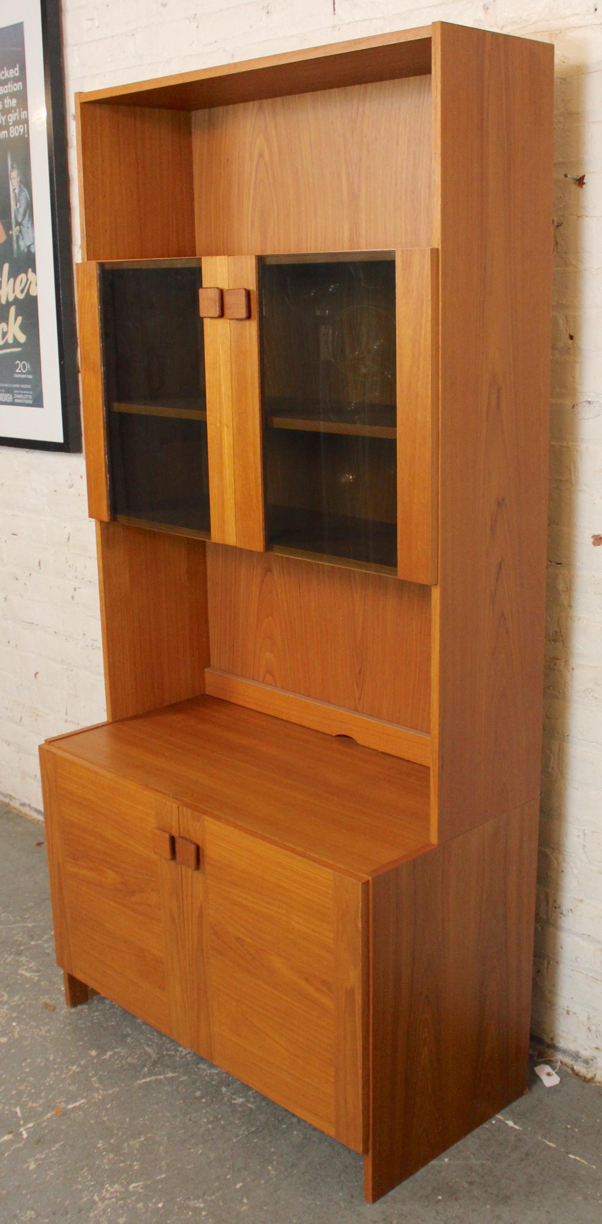 Armadietto a due ante in teak di produzione danese con un topper libreria dotato di un mobile a due ante in vetro fumé. Questo mobile a due pezzi offre un grande spazio di archiviazione con un fascino moderno.
Si prega di confermare l'ubicazione con