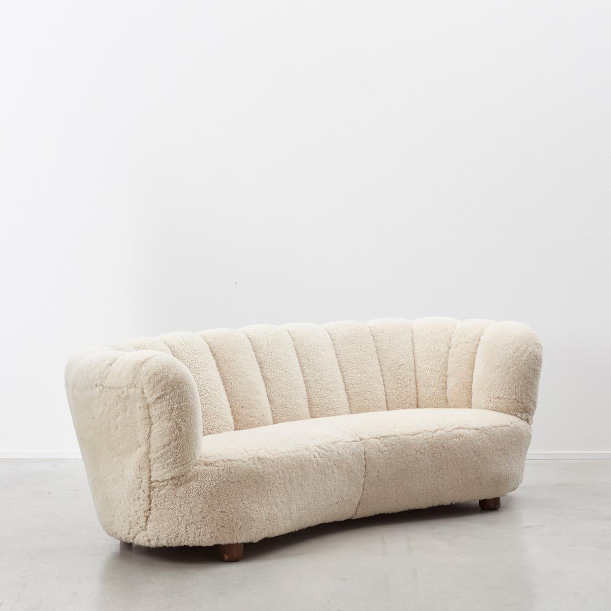 Early 1940s Danish Banana three-seat sofa in the manner of architect Flemming Lassen, newly reupholstered in genuine sheeps pelts. The sofa is of excellent craftsmanship, probably made by Slagelse Møbelværk, Denmark using proper materials – solid