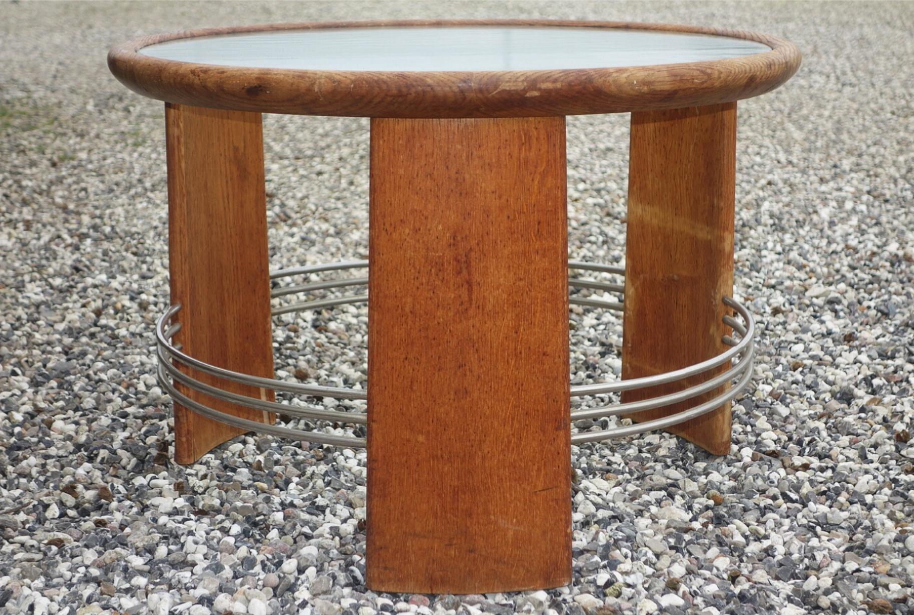 Circular Art Deco coffee table of oak with metal rails. Top of glass. Made 1930s-1940s. Measures: Height 50 cm., diameter 75 cm.
Wear of age and wear, including scratches, marks, damp marks, drying cracks and veneer damages on legs.
          