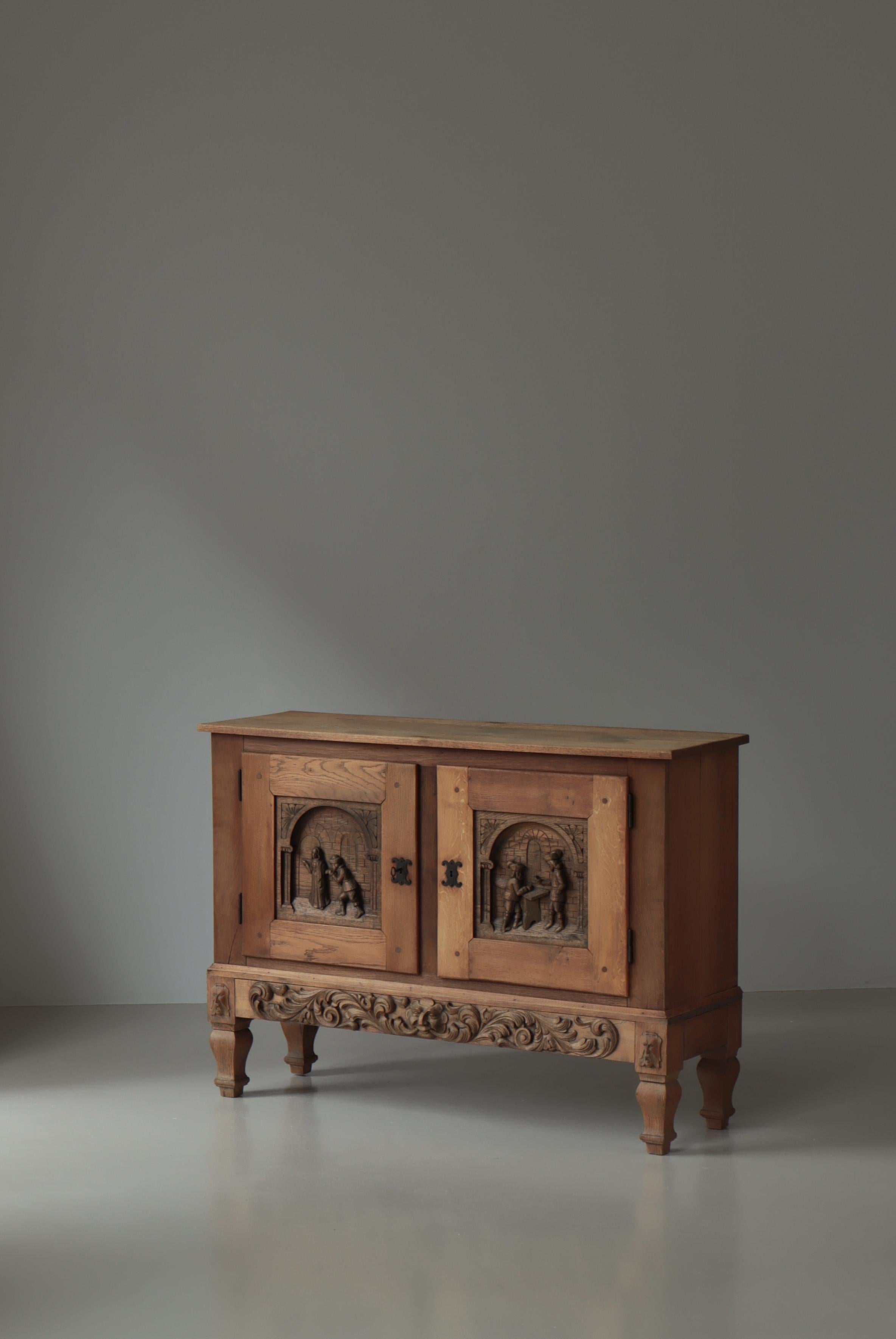 Precioso armario grueso de madera de roble fabricado por un ebanista danés en la década de 1920. Maravillosos motivos tallados a mano con temas de mediana edad en la parte frontal de las puertas. Patas de estilo barroco. Llave y cerradura de hierro