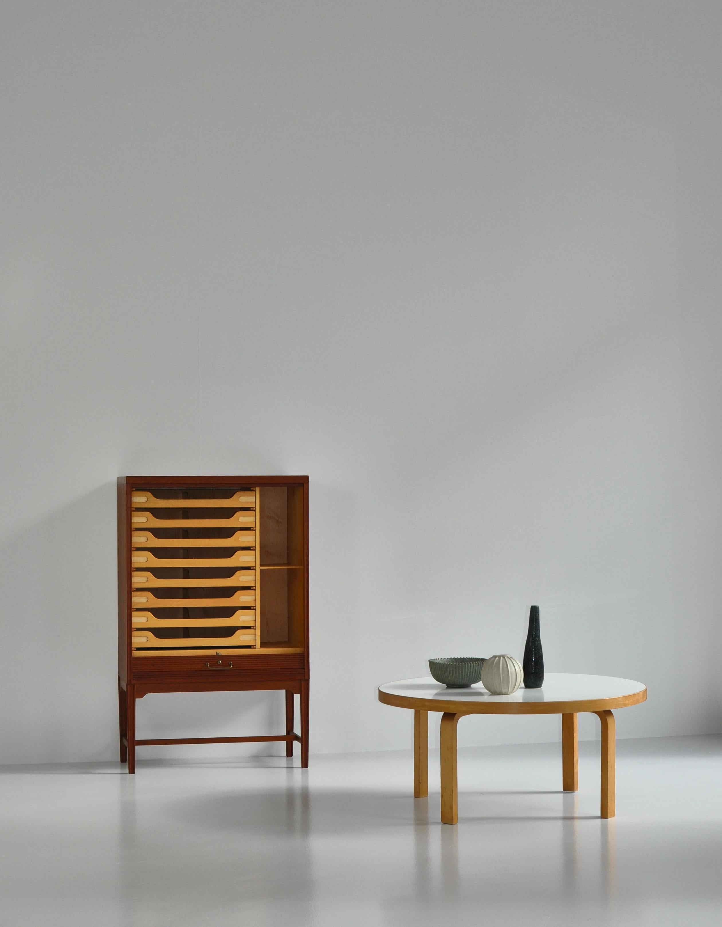 Made in the 1950s by Danish cabinetmaker this beautiful cabinet features smooth front tambour door that roll down into the base and out of sight and eight shallow drawers made of beechwood. In the style of Hvidt & Mølgaard, Jacob Kjaer and other