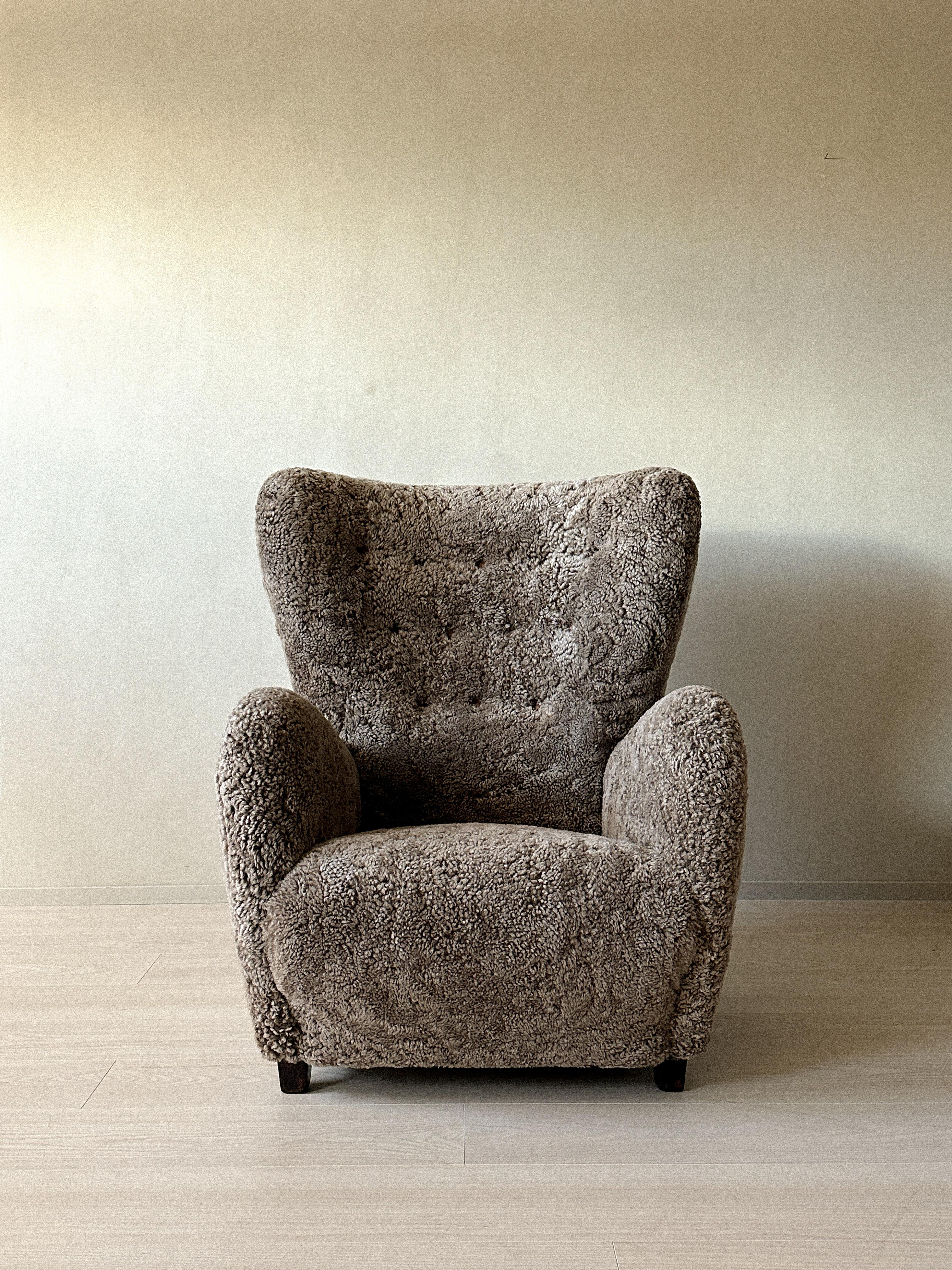 A 1940s Danish Cabinetmaker wing back lounge chair with beautiful curves. The chair is newly reupholstered in premium shearling and leather buttons.