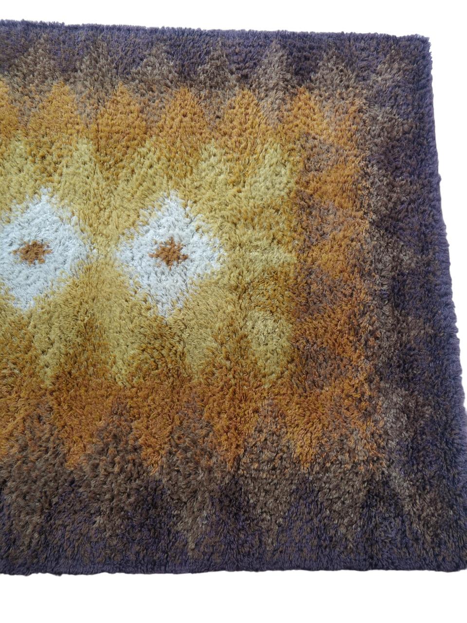 This rug, crafted using the Rya weaving technique in Denmark, is an expression of Nordic design. Made entirely of pure wool, it features a variety of tones ranging from beige to brown, with a diamond pattern in the center on a light background that