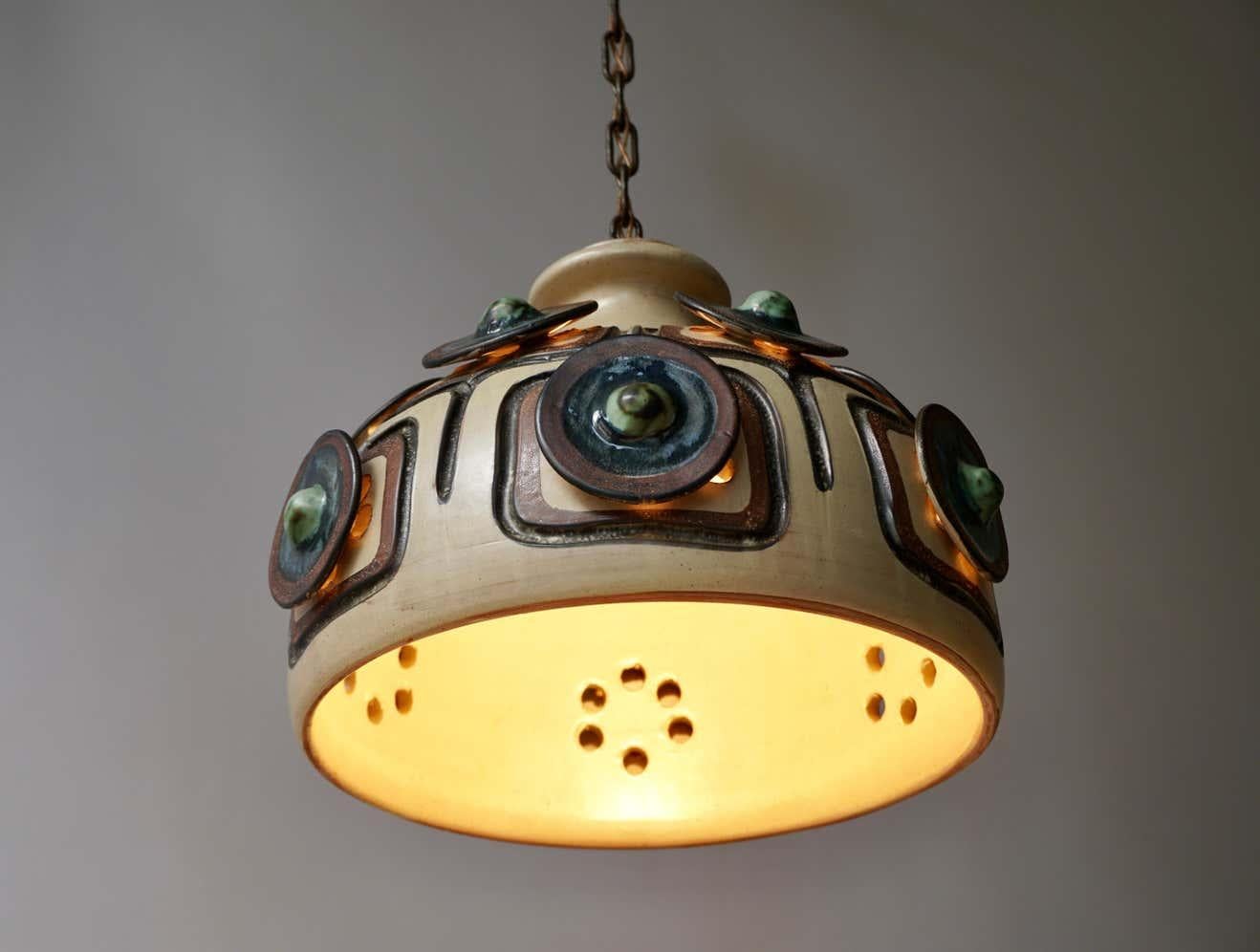 Handmade Danish ceramic chandelier / pendent lamp, made by Jette Hellerøe for Axella in ca. the 1970s. The piece shows a mix of beige, blue, brown and green colors. The Lamp features round decorated discs from where the lights shines through as also