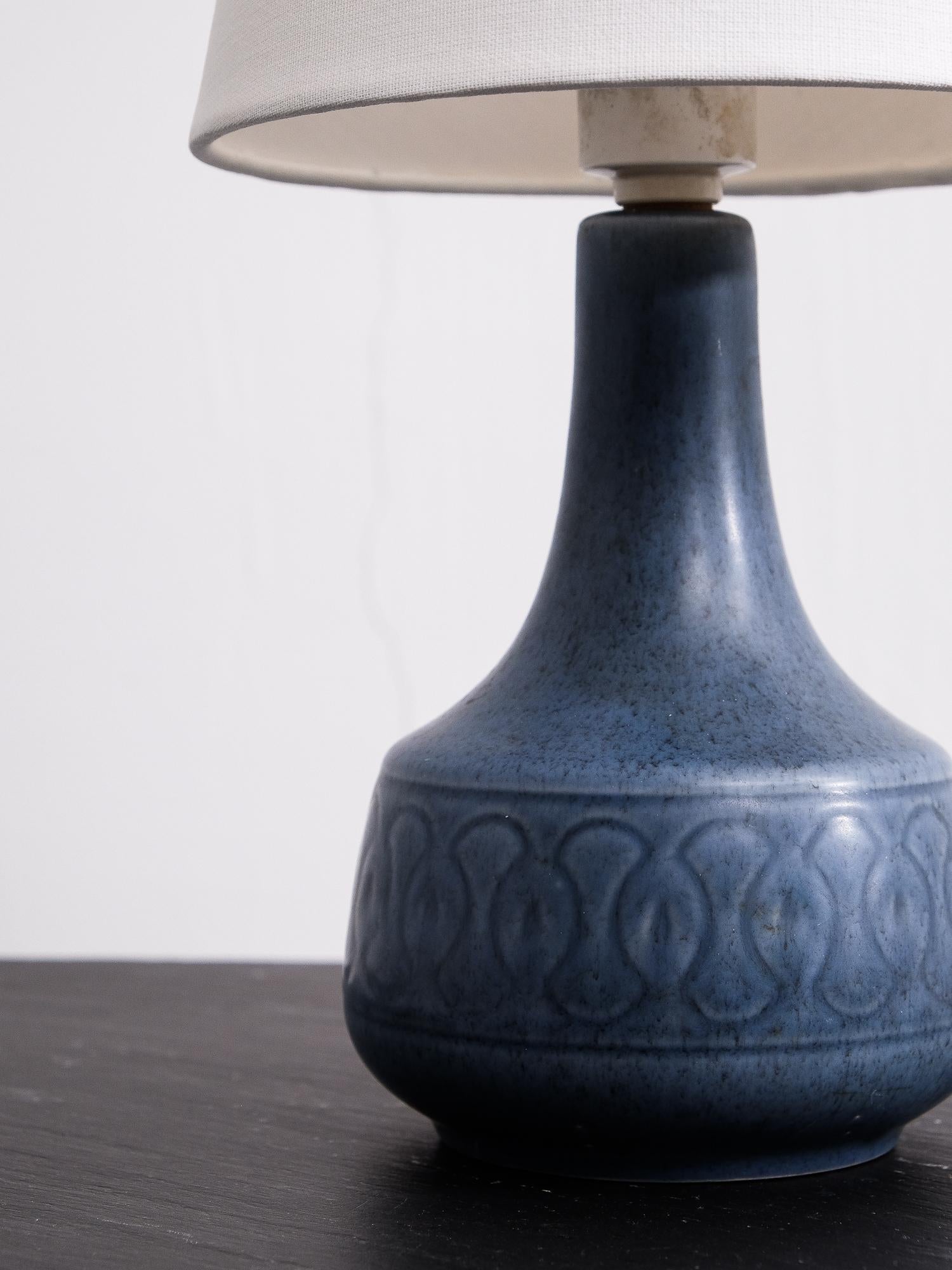 Danish handmade table lamp with ceramic glazing in tones of blue. Graphical pattern to the base of the lamp. The lamp has been rewired for European use and has a new shade.

E27 bulb holder
Measures: Height with shade 35 cm.
