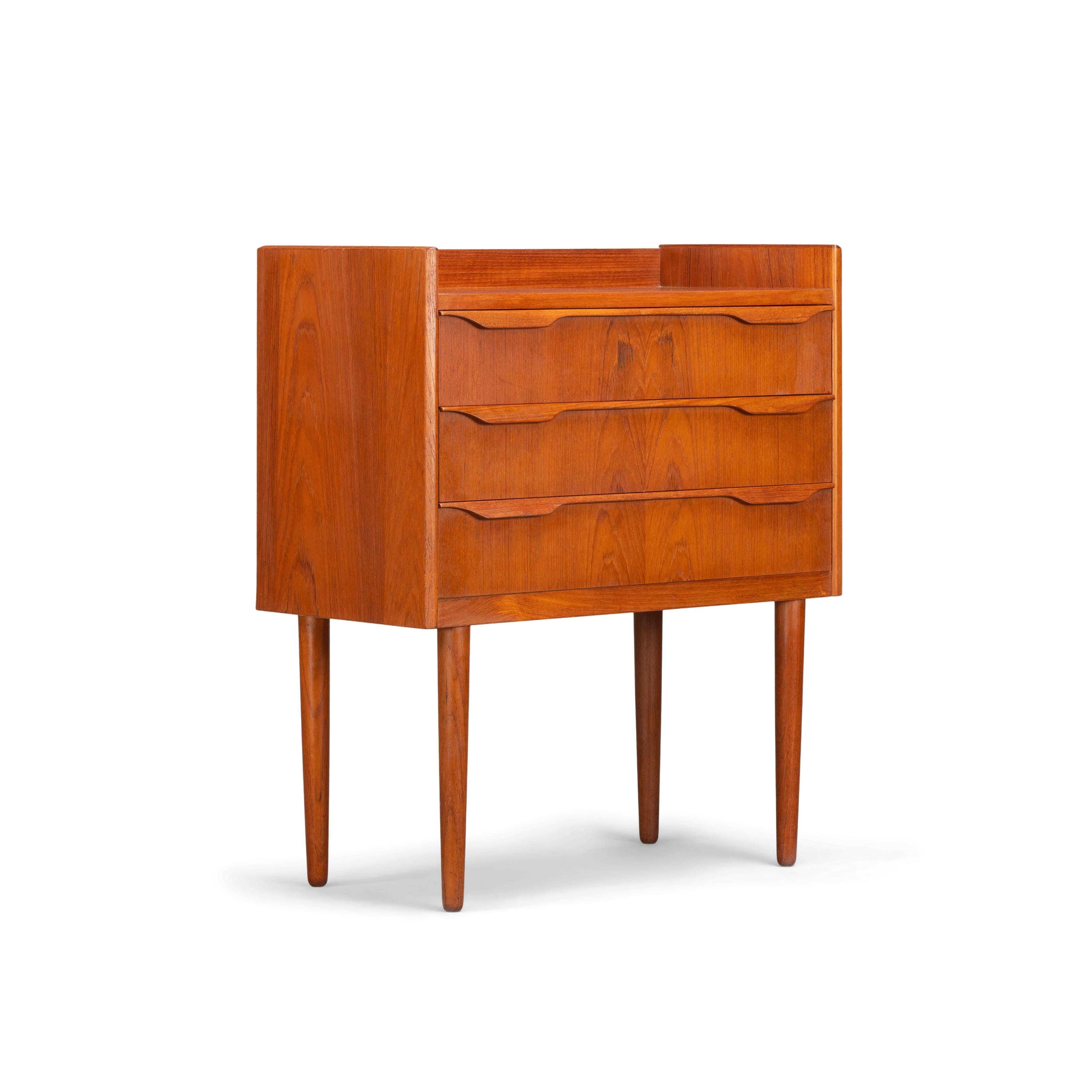 This Danish nightstand in teak veneer was made late 1960s and looks very charming on its tall solid teak legs. Three drawers with a solid wooden grip attached onto the middle of each drawer makes the style of this nightstand complete. Unfortunately
