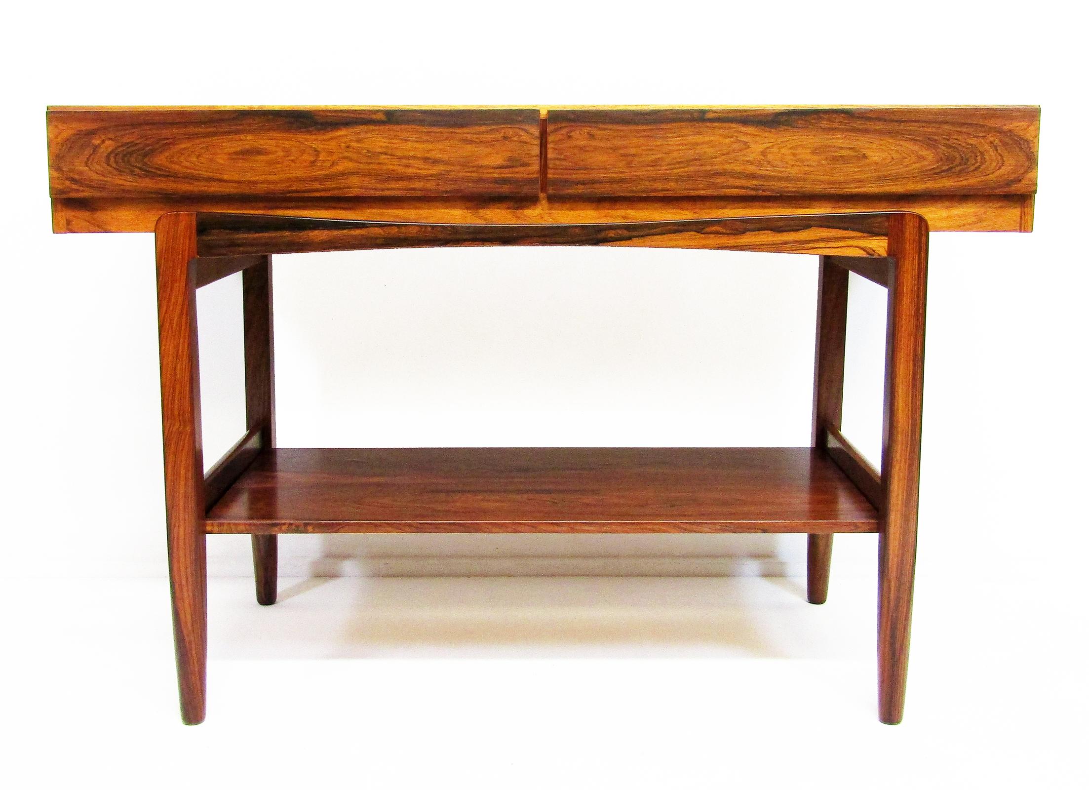 A Danish rosewood console table with two drawers, undertier and distinctive curved leg supports by Ib Kofod Larsen for Faarup Mobelfabrik. The Faarup sticker is affixed to the rear.

This rare adapted version has a removeable undertier,  allowing it