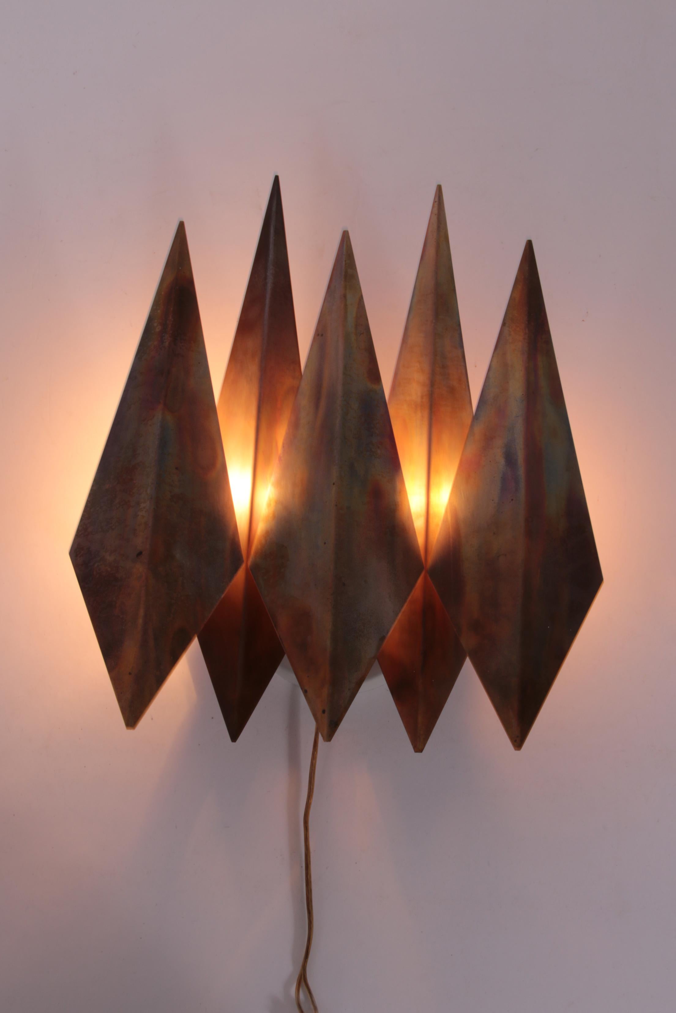 Cette étonnante applique, conçue dans les années 1970 par Sven Aage Holm Sørensen et produite par sa société Holm Sørensen A/S, présente une forme de diamant distinctive fabriquée à partir de métal brut. Bien qu'elle soit aujourd'hui communément