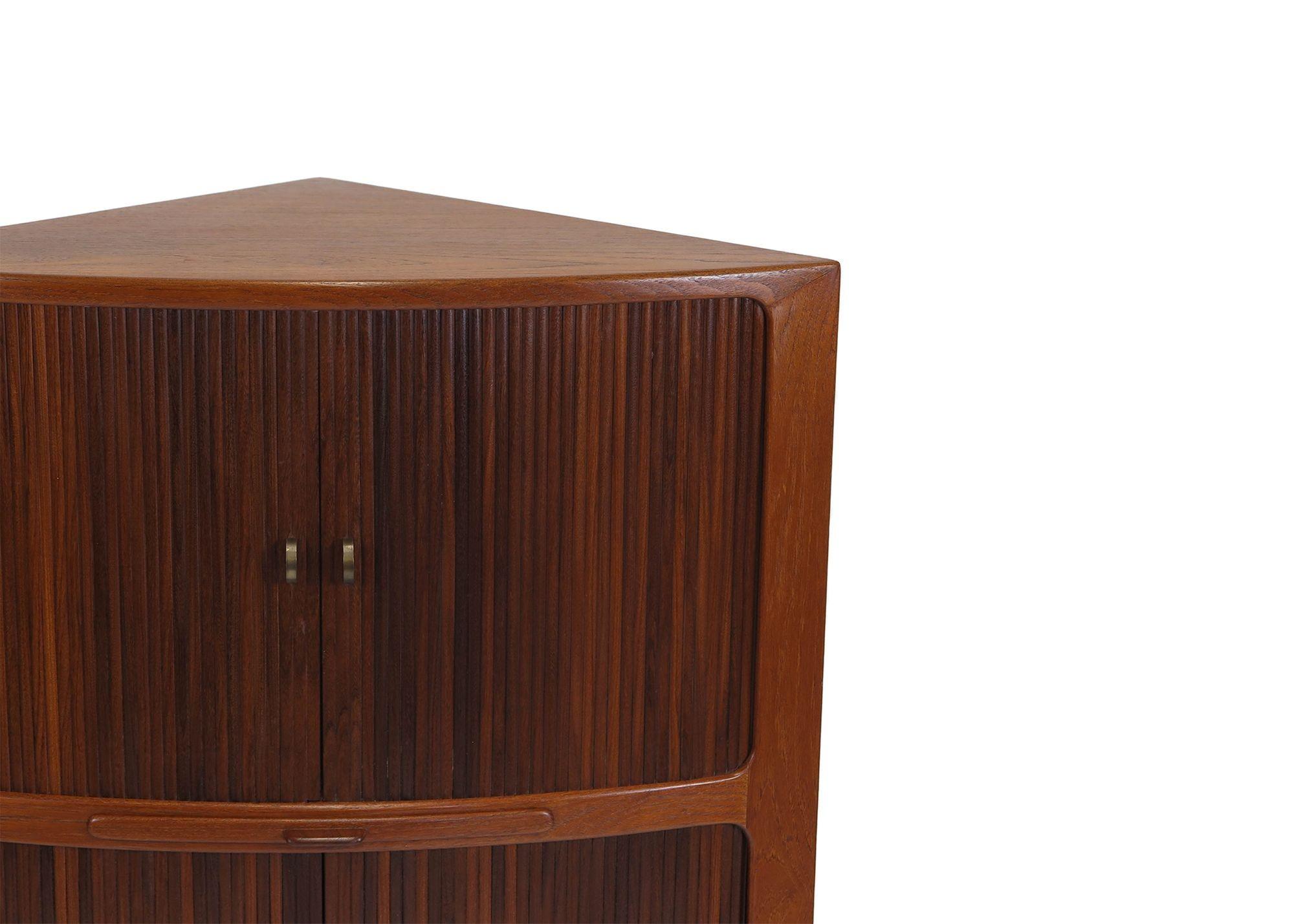 Midcentury Teak corner cabinet attributed to Danish designer, Johannes Andersen. The cabinet is crafted of teak with two sections of tambour doors. The upper section reveals an interior with an etched mirror back, black glass base, shelf and