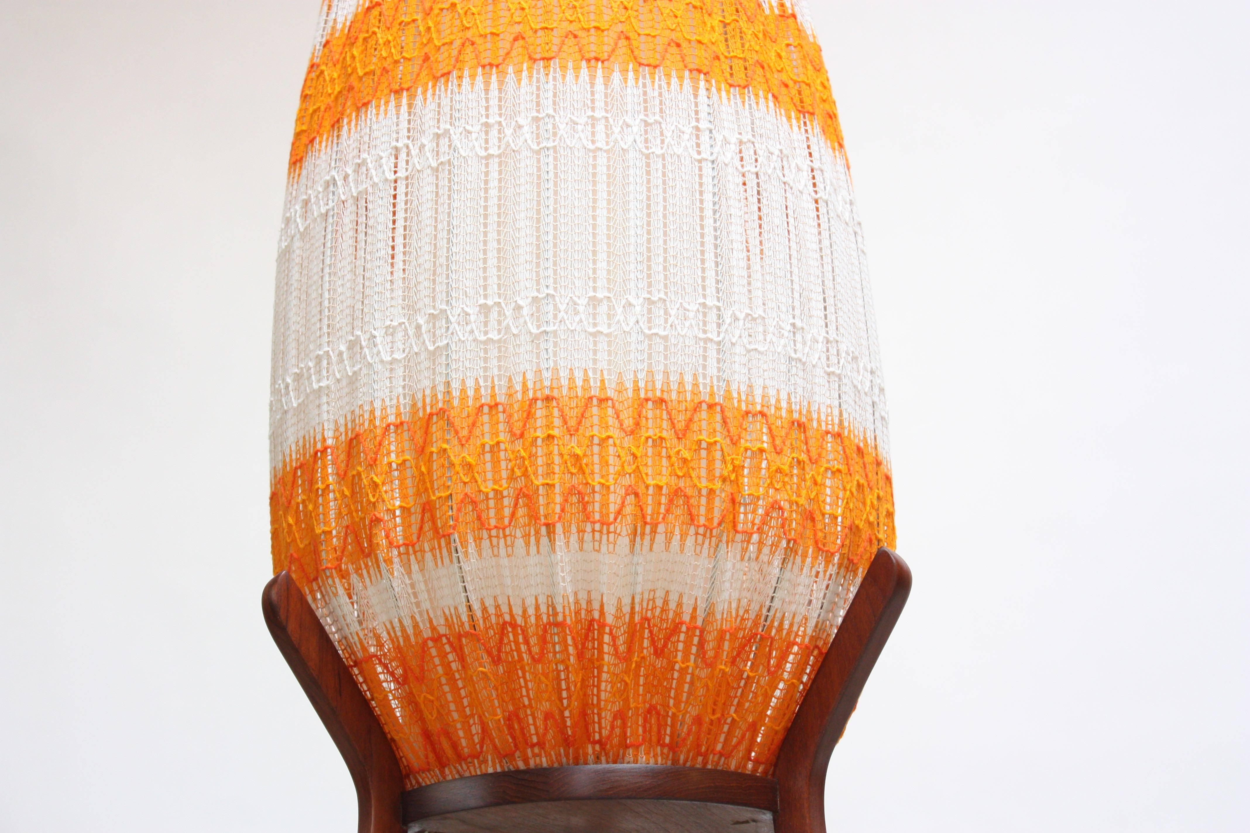 This 1960s Danish floor lamp is composed of an exterior orange and white linen shade with a crocheted pattern. (There is a parchment inner shade that is connected to the steel form body that the linen shade conceals.) The tripod base is teak, and