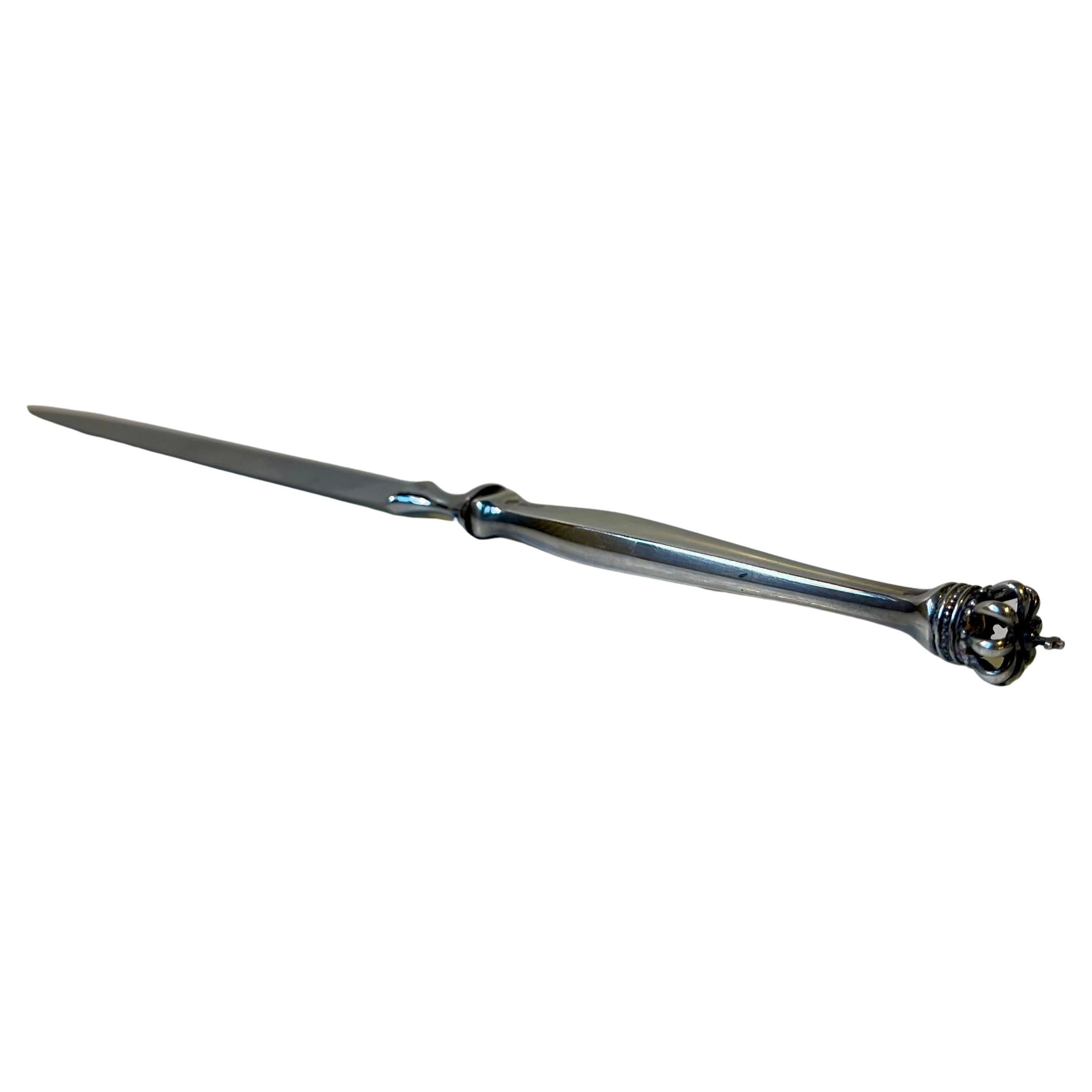 Ein stilvolles Papiermesser mit länglichem Griff aus Sterlingsilber, auf dem die dänische Königskrone abgebildet ist, daher auch der Name Dänische Krone oder Dansk Krone auf Dänisch. Vollständig hallmarkiert.  

Abmessungen: 22x1,5x1,5 cm.