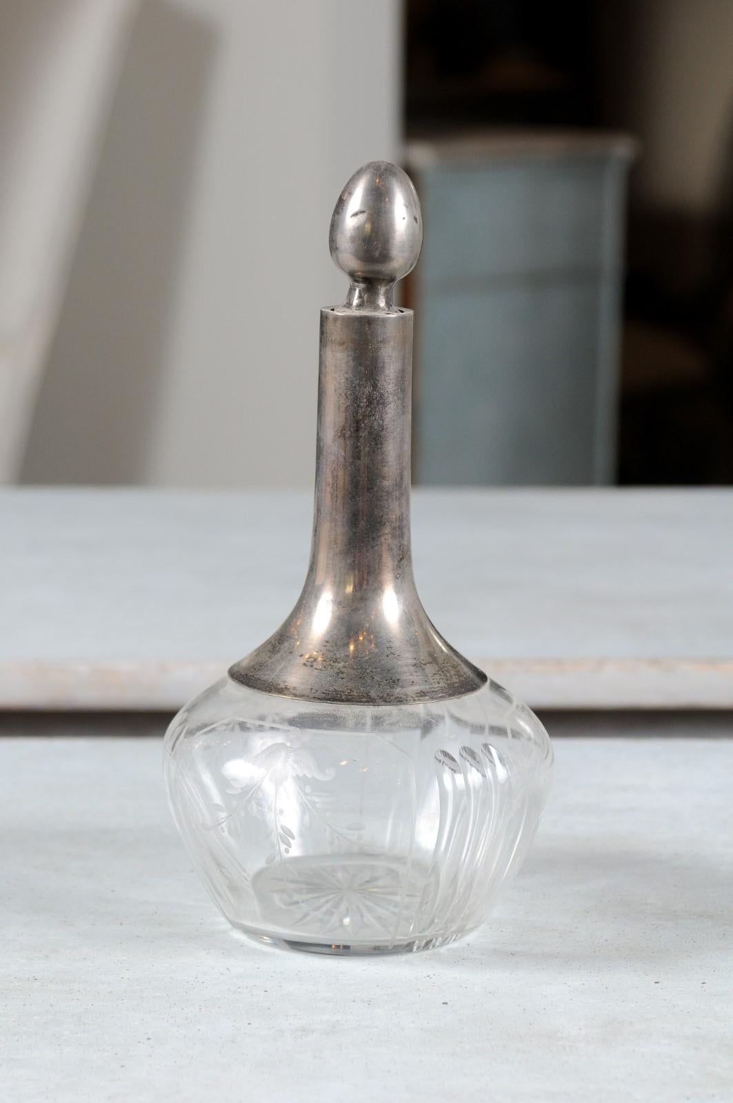 A Danish crystal and silver decanter from the 20th century, with acorn-shaped stopper and engraved foliage motifs. Born in Denmark during the 20th century, this decanter features a slender silver neck topped with a stopper and sitting above a