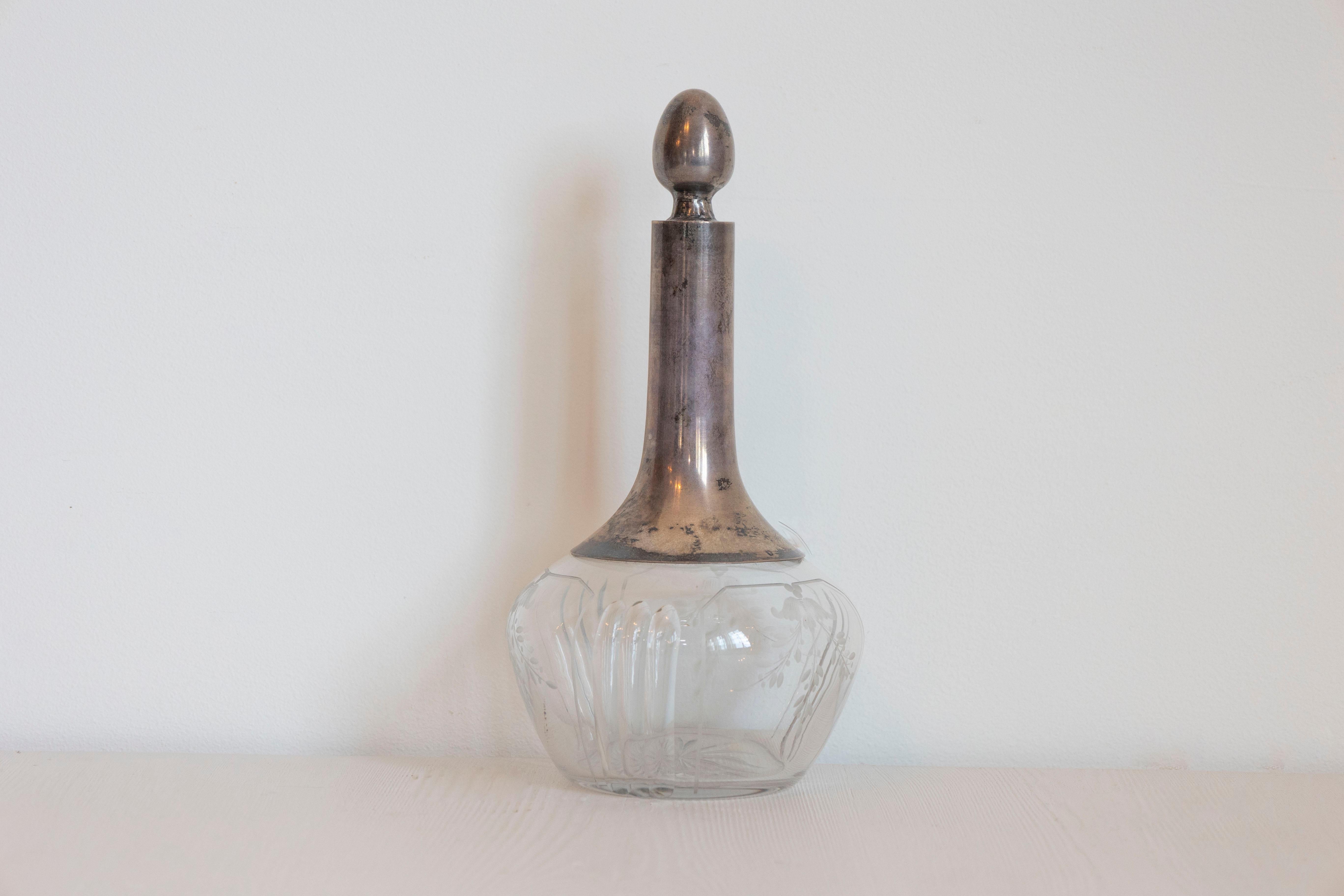 Decanter danese in cristallo e argento del XX secolo, con tappo a forma di ghianda e motivi di fogliame incisi. Nato in Danimarca nel XX secolo, questo decanter presenta un sottile collo d'argento sormontato da un tappo e posto sopra un corpo