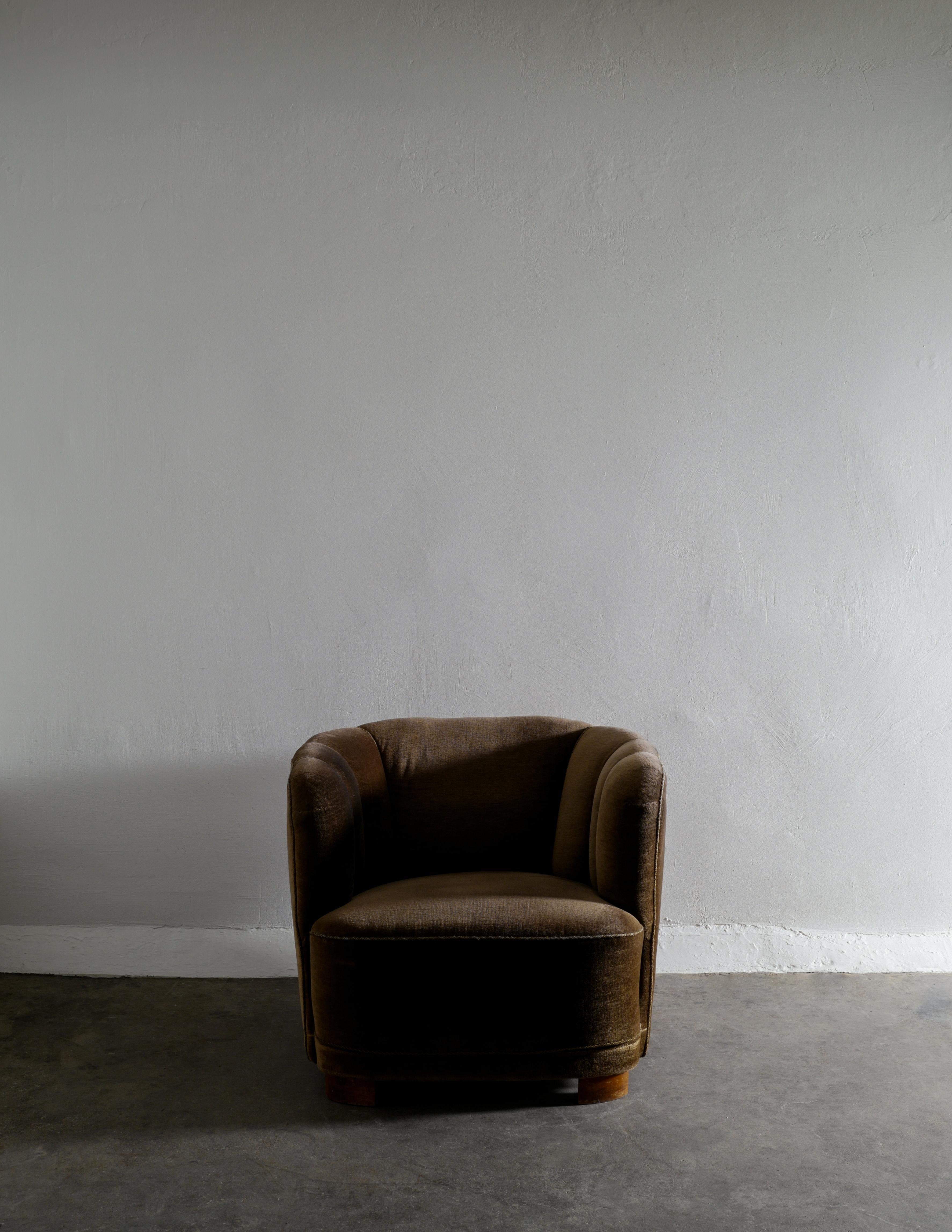 Rare curved easy chair produced in Denmark in the 1940s by unknown designer. Original velour fabric in a green / brownish color and beech feet. Attributed to Flemming Lassen and Viggo Boesen. 

Dimensions: H: 67 cm W: 79 cm D: 85 cm SH: 39 cm.