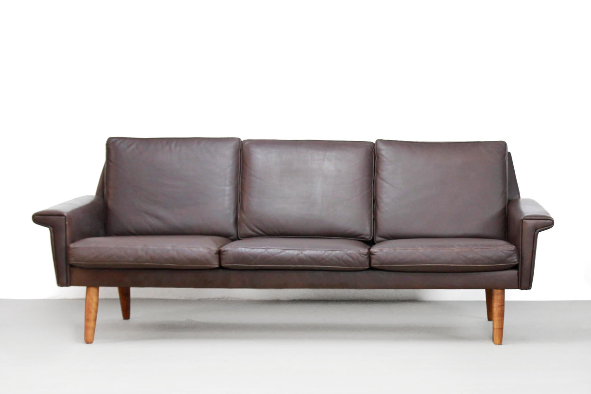 Dark brown leather Danish design sofa, produced by Vejen Polstermobelfabrik from Denmark. This three-seat is made of brown leather with conical light wooden legs. The sofa has a very beautiful midcentury modernist design which appearance does not