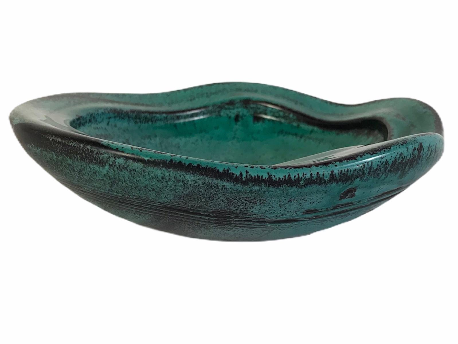 Danish designer Svend Hammershoi created this low freeform ceramic bowl in the 1930s for Kahler Keramiske. Beautiful vessel in mottled malachite green with black brown outline and a fluid undulating edge. Incised bands and concentric circles design