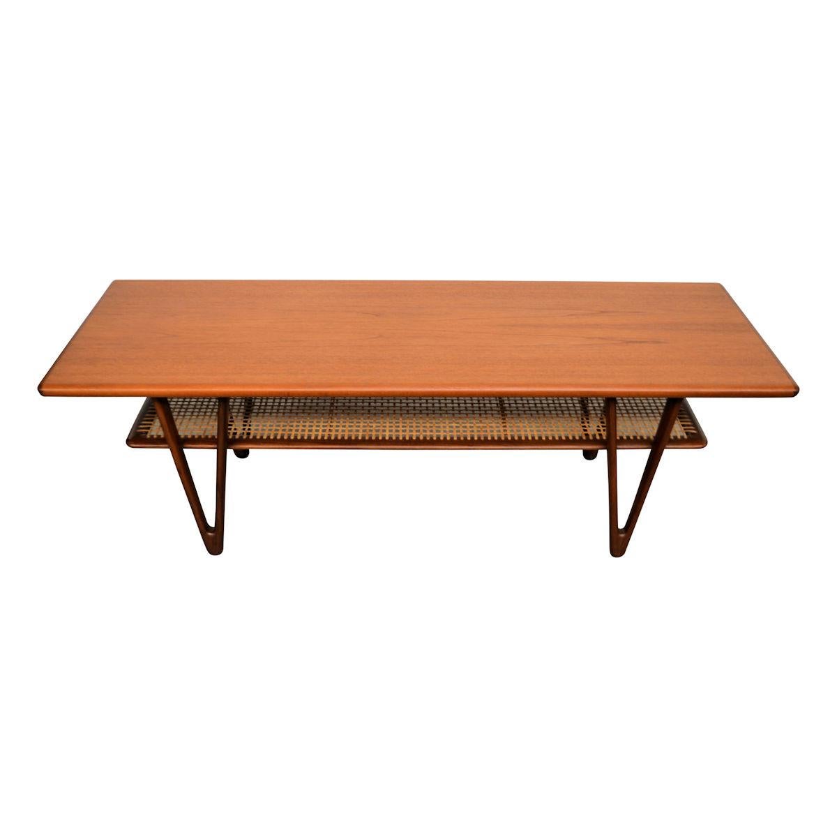 Gorgeous Danish design teak vintage coffee table in the style of Kurt Østervig. The table features beautiful rounded table top on corners. the stunning triangle legs and a ratan storage shelf for magazines and newspapers and such. A beautiful