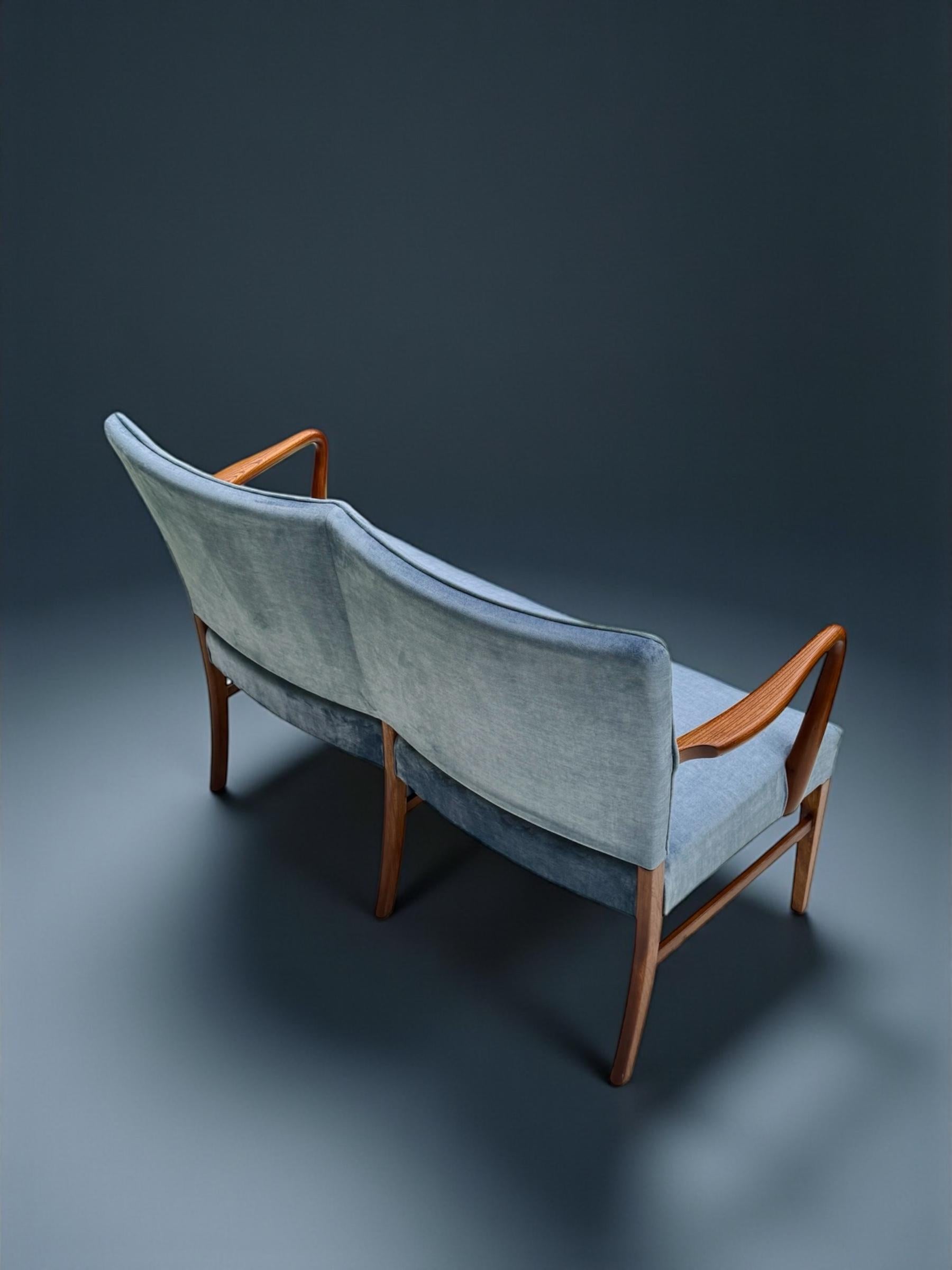 In the manner of Finn Juhl this settee has huge charm both in the form and treatment of the comfortable arm rests and the combination of the velvet upholstery adding colour and comfort for a statement piece in your decor.