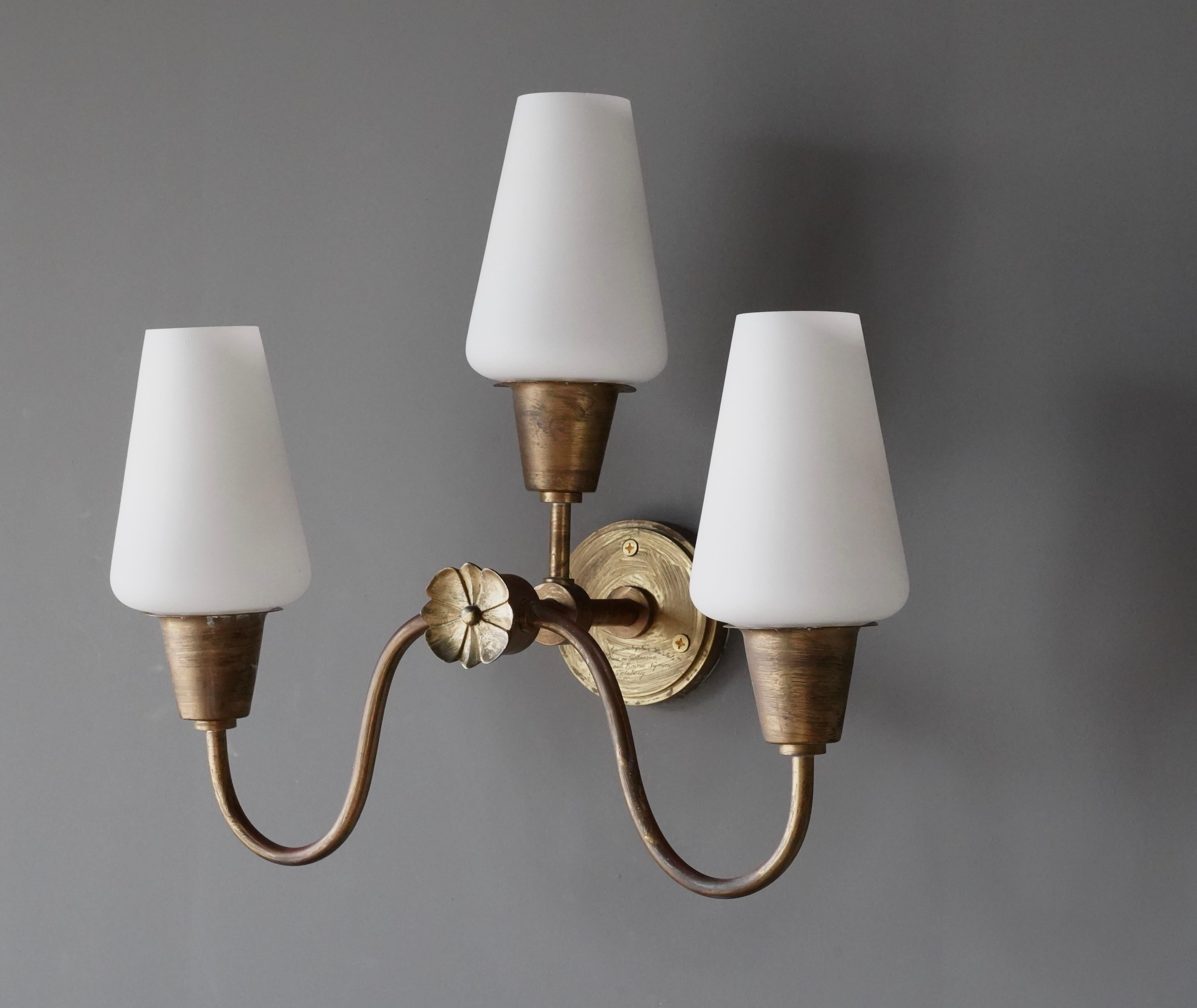 A three armed wall light. Designed and produced in Denmark, c. 1930s-1940s. Features brass and milk glass.

Fixture presents with dramatic and beautiful patina.

Three arm brass wall light with frost glass. Engraved on the front of base. Patina