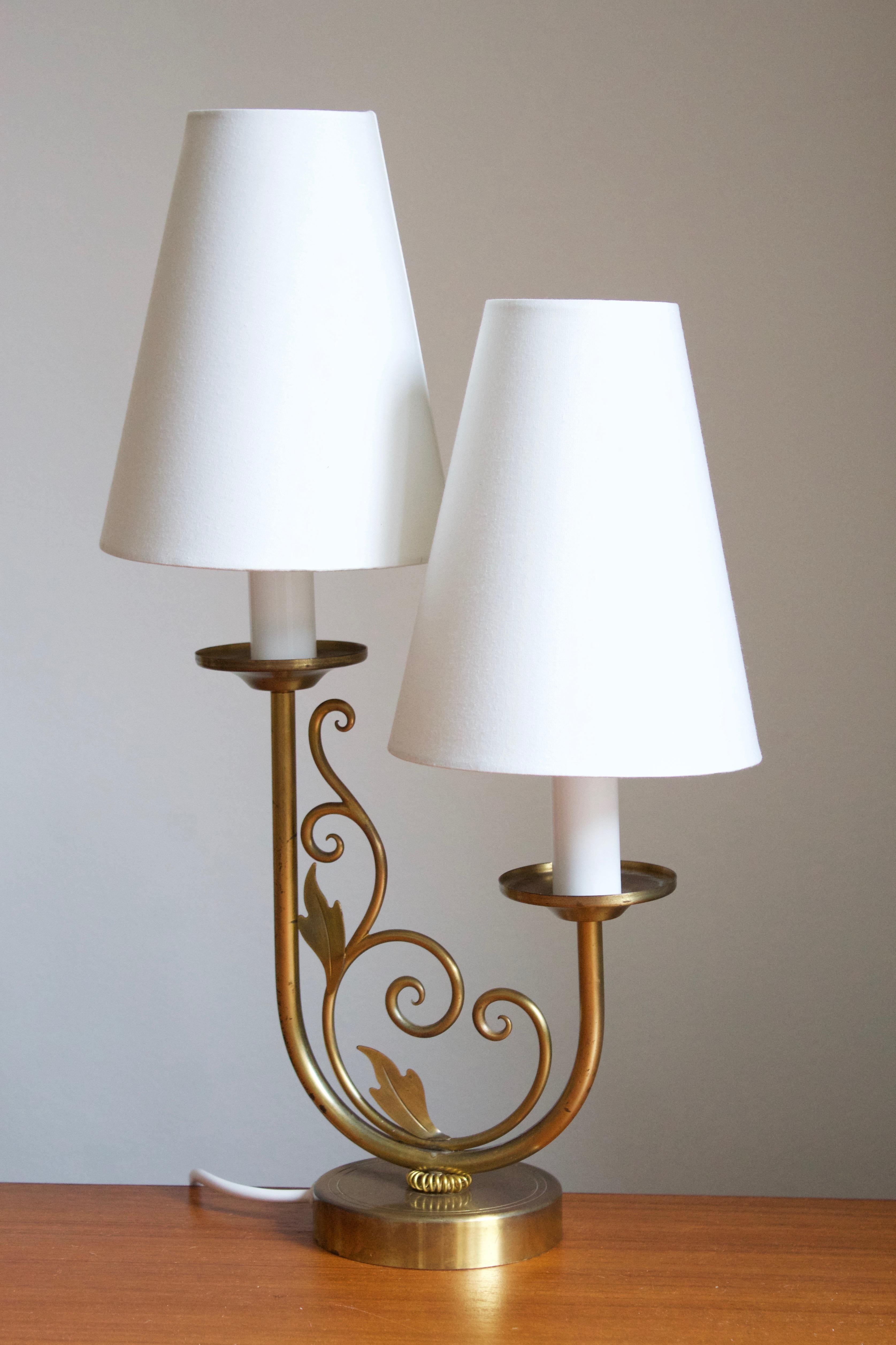 A two-armed table lamp. Designed and produced in Denmark c. 1940s-1950s. Features organic ornamentation and a brass ribbon. 

Stated dimensions include lampshades as illustrated. Sold without lampshades.

 
