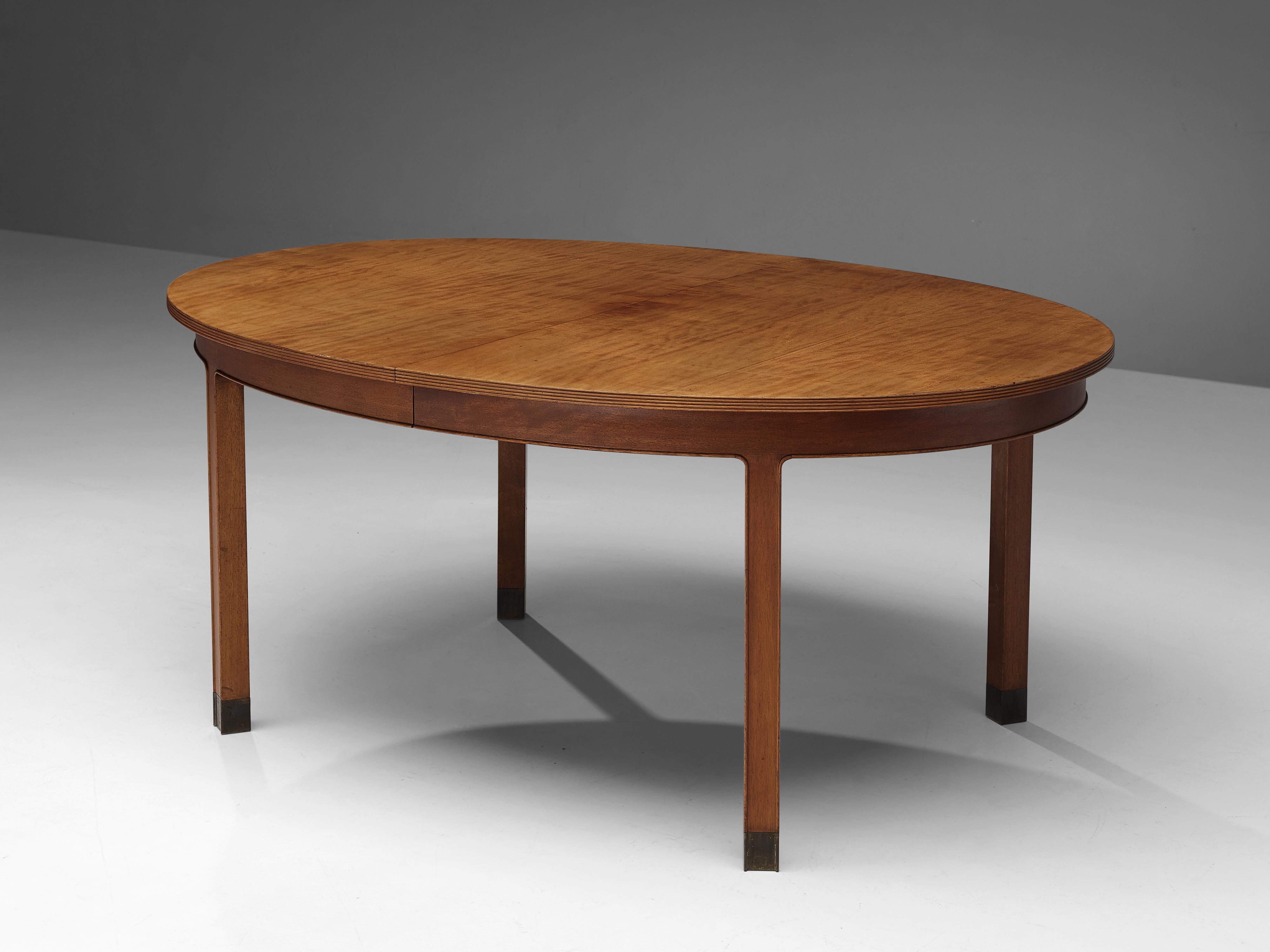 Dining table, mahogany, walnut, brass, Denmark, 1950s.

This elegant dining table has a wonderful oval top resting on four legs with carved edges and brass feet. Underneath the tabletop a functional and thought-through mechanism can be found that