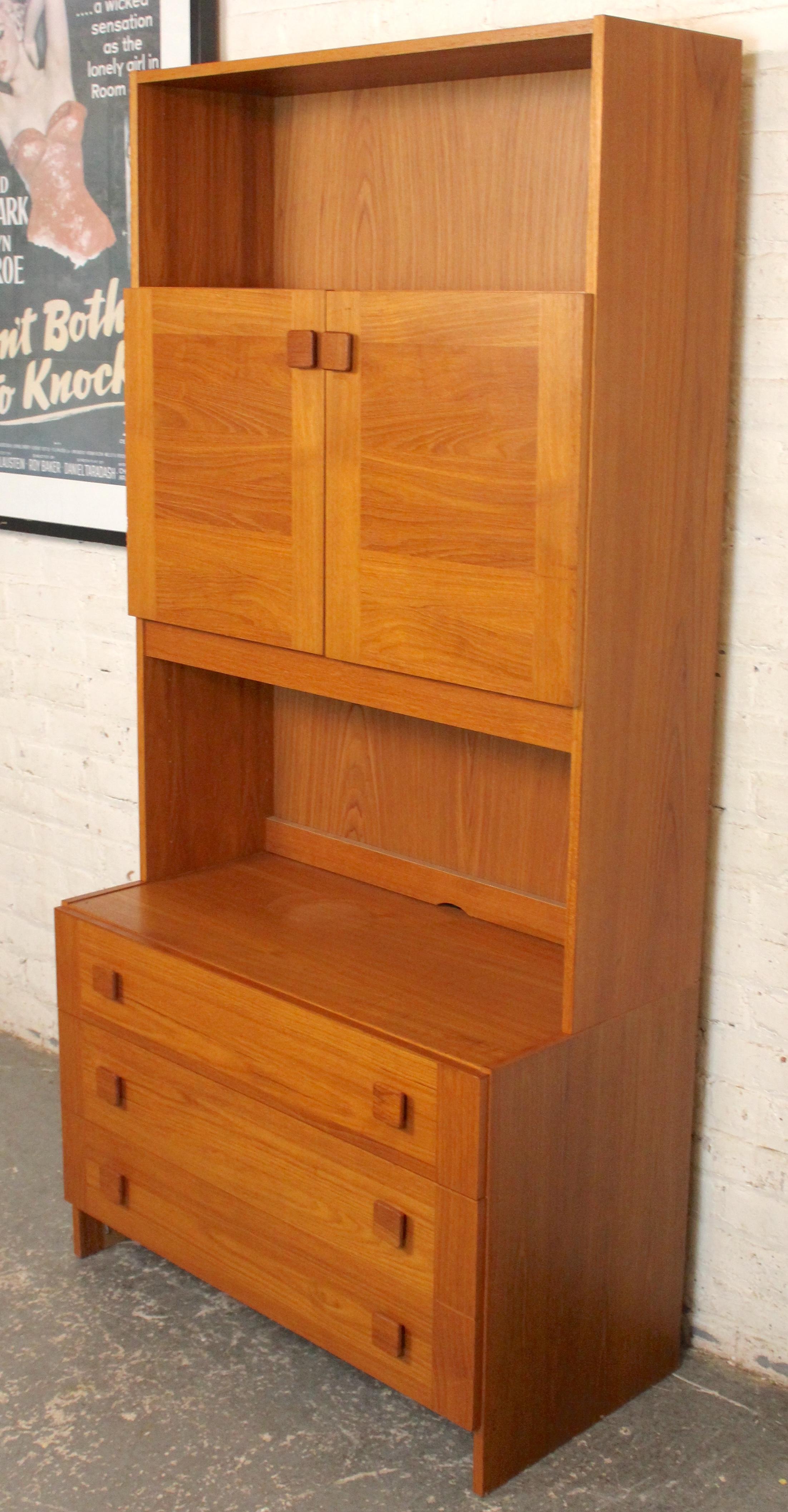 Questo mobile in teak di produzione danese racchiude una grande quantità di spazio in un ingombro ridotto. Una cassettiera alla base con un mobile libreria a due ante sulla parte superiore. 
Si prega di confermare l'ubicazione con il venditore NY o