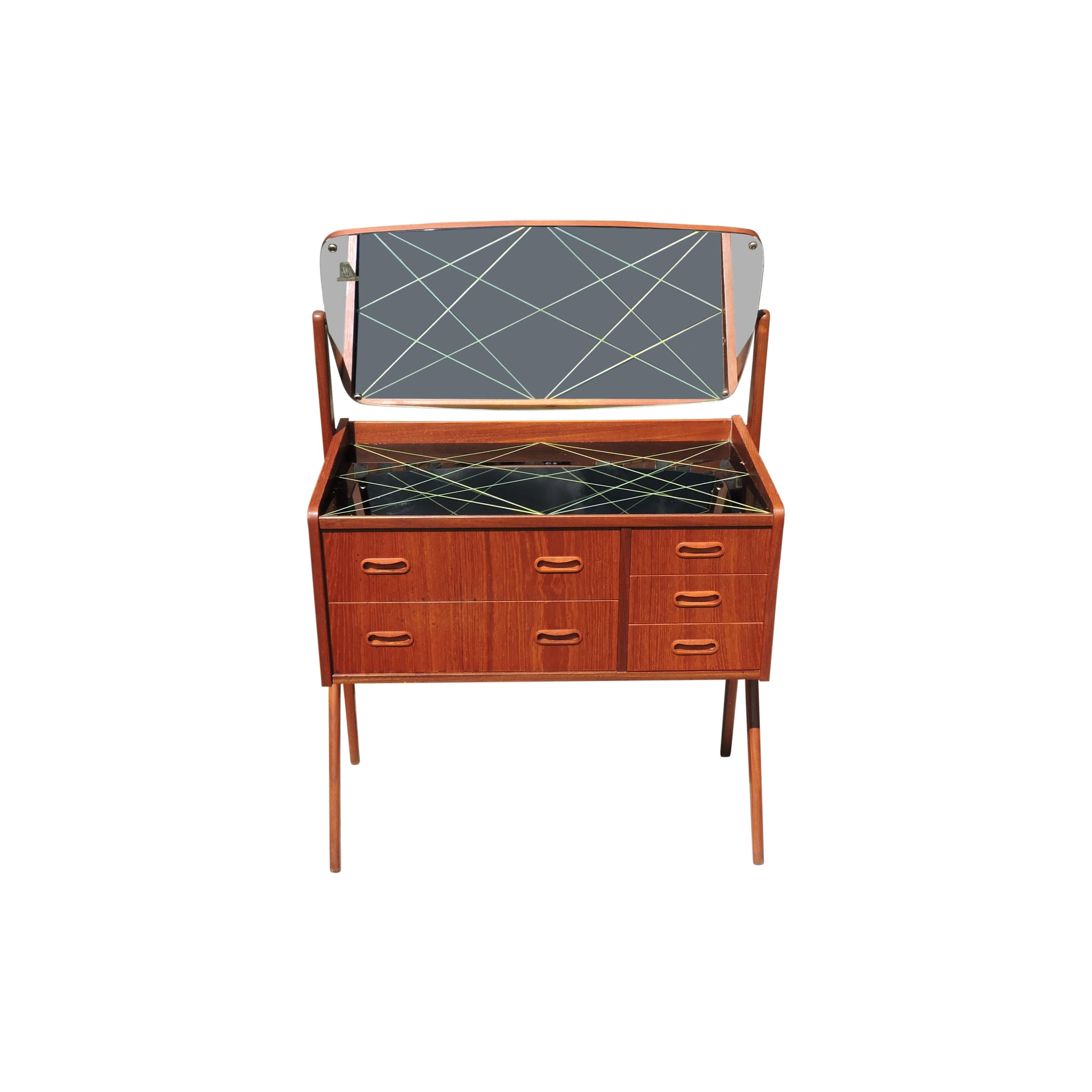 This Danish dressing table is made in teak veneer. The mirror is an oval shape and the drawers are of different sizes. It features a glass top with a geometric pattern.