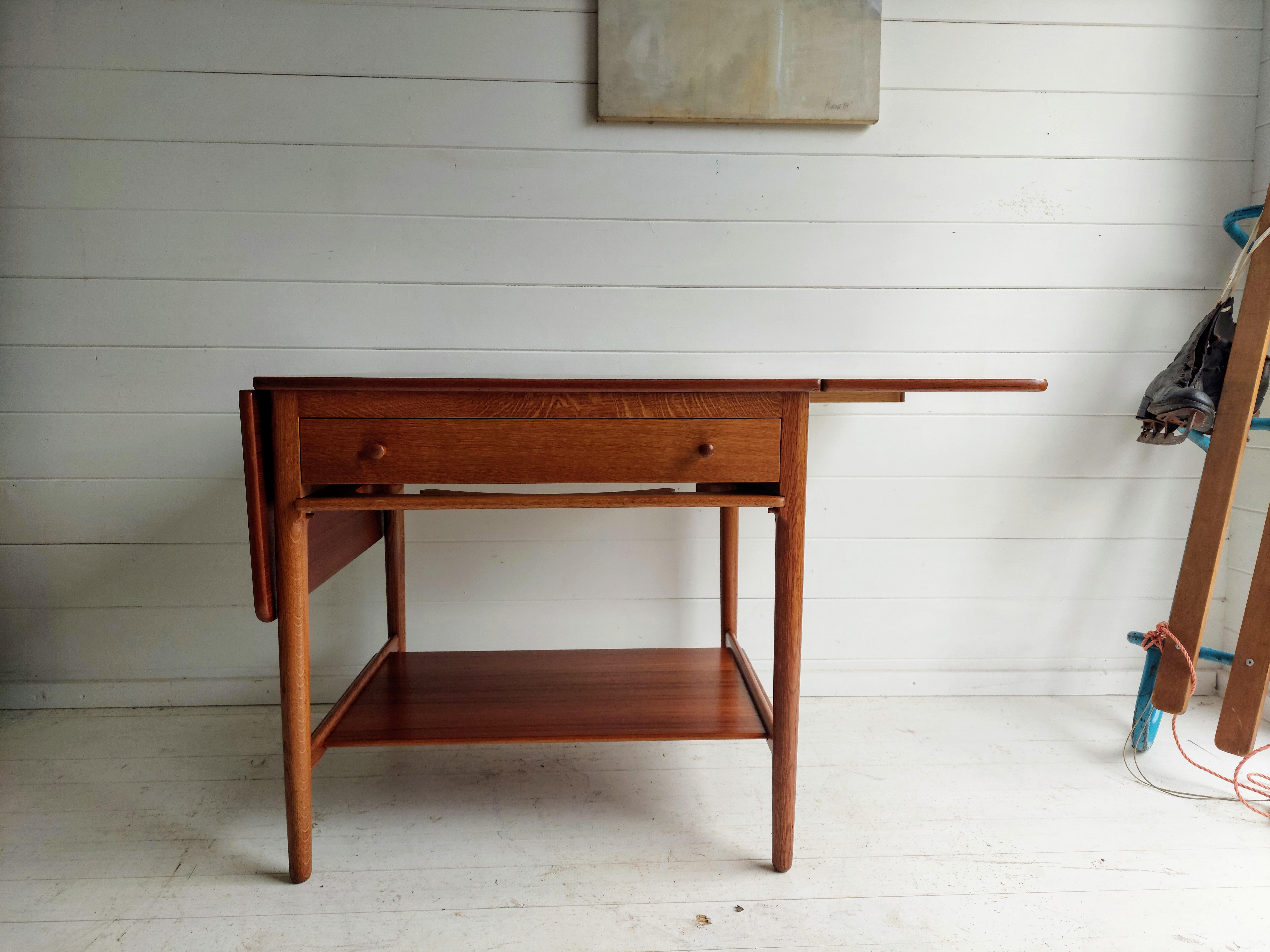 1950s Danish solid teak sewing or side table (model AT33) designed by Hans J Wegner and manufactured Andreas Tuck.

Crafted with two drop leaves that extend the table from 66cm to 118 cm maximum length.
The drawer, boasting sculptural teak pulls,