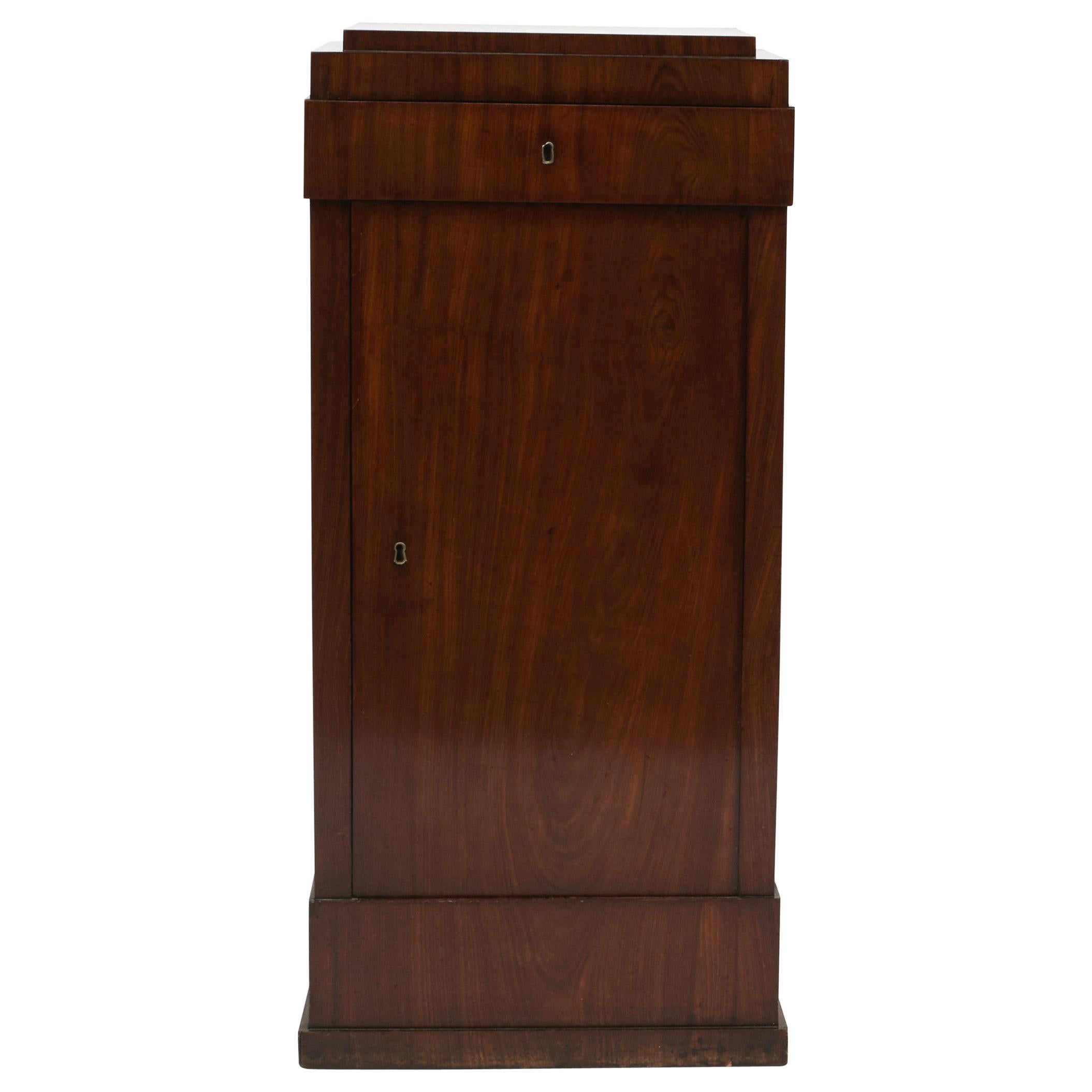 A handsome Danish Empire pedestal cabinet. Made in mahogany with beautiful wood grain.
This cabinet offers a storage drawer above a door, that opens to reveal three shelves.
Drawer with label from The Furniture Emporium of United Artwork (“Det