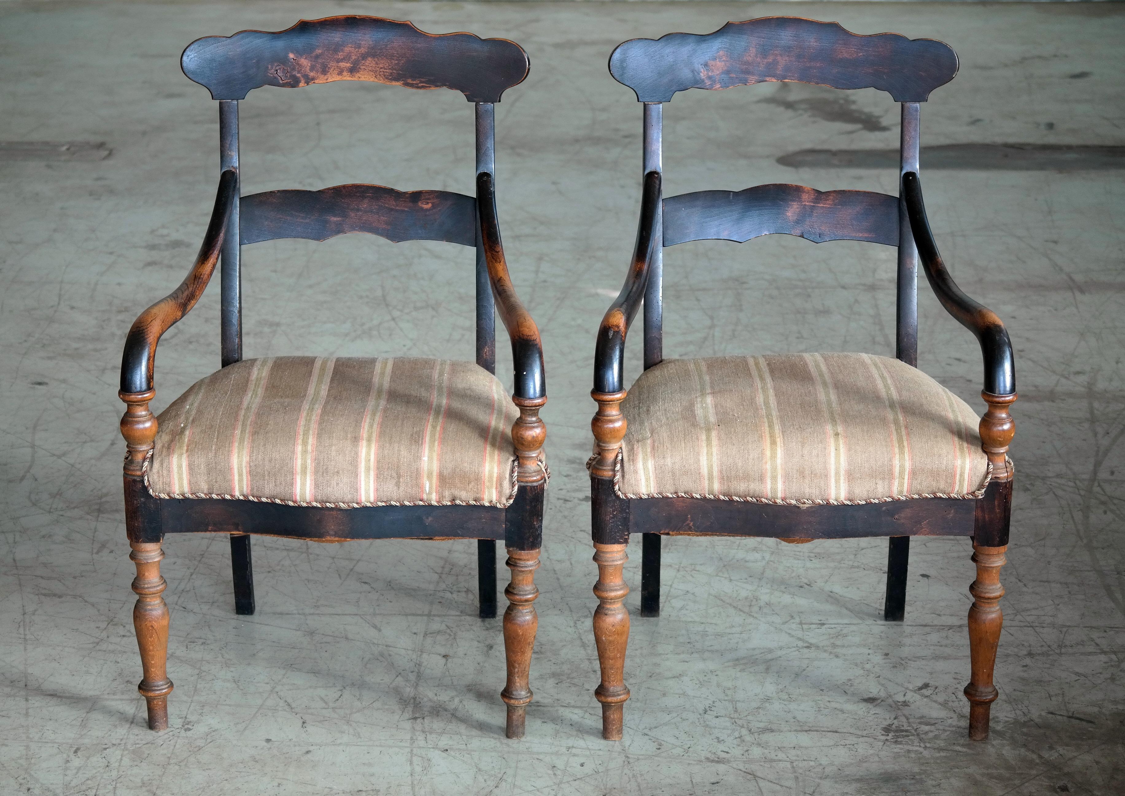 Great pair of country style armchairs made in Denmark in the early part of the 20th century. Hand carved from solid oak and stained. Over time the chairs have achieved an absolutely remarkable patina showing wear the to armrests. The fabric is worn