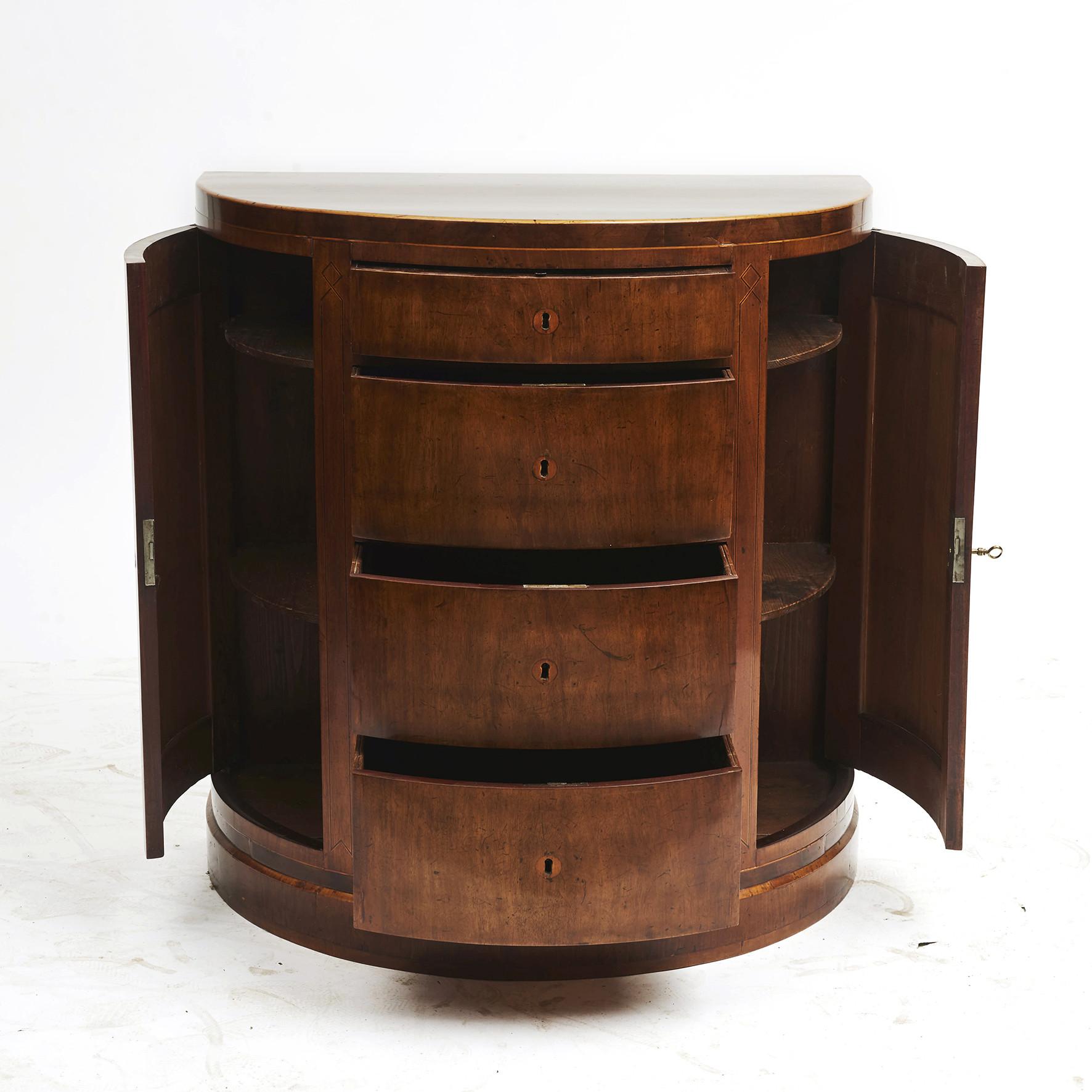Danish empire demilune commode or cabinet in mahogany.
4 central drawers flanked by cupboard doors.
Top drawer with pull-out writing surface.
Half round top with inlays in satinwood. Doors with marquetry in dark and light wood.
Copenhagen,