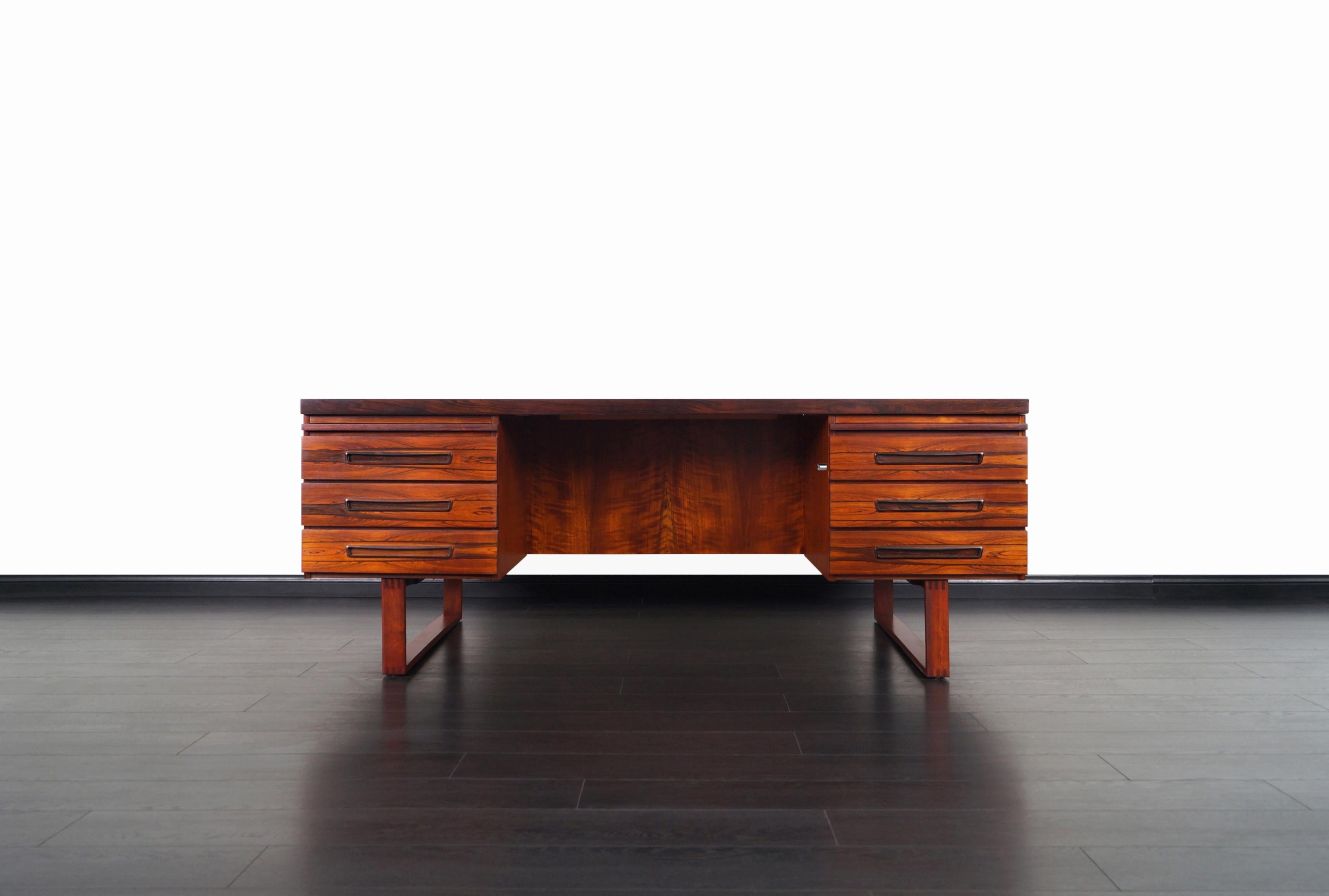 Danish modern executive rosewood desk designed by Henning Jensen and Torbin Valeur for Dyrlund in Denmark, circa 1960s. This desk features a stunning Brazilian rosewood case that sits over a pair of sleigh legs, with six dovetailed drawers and two