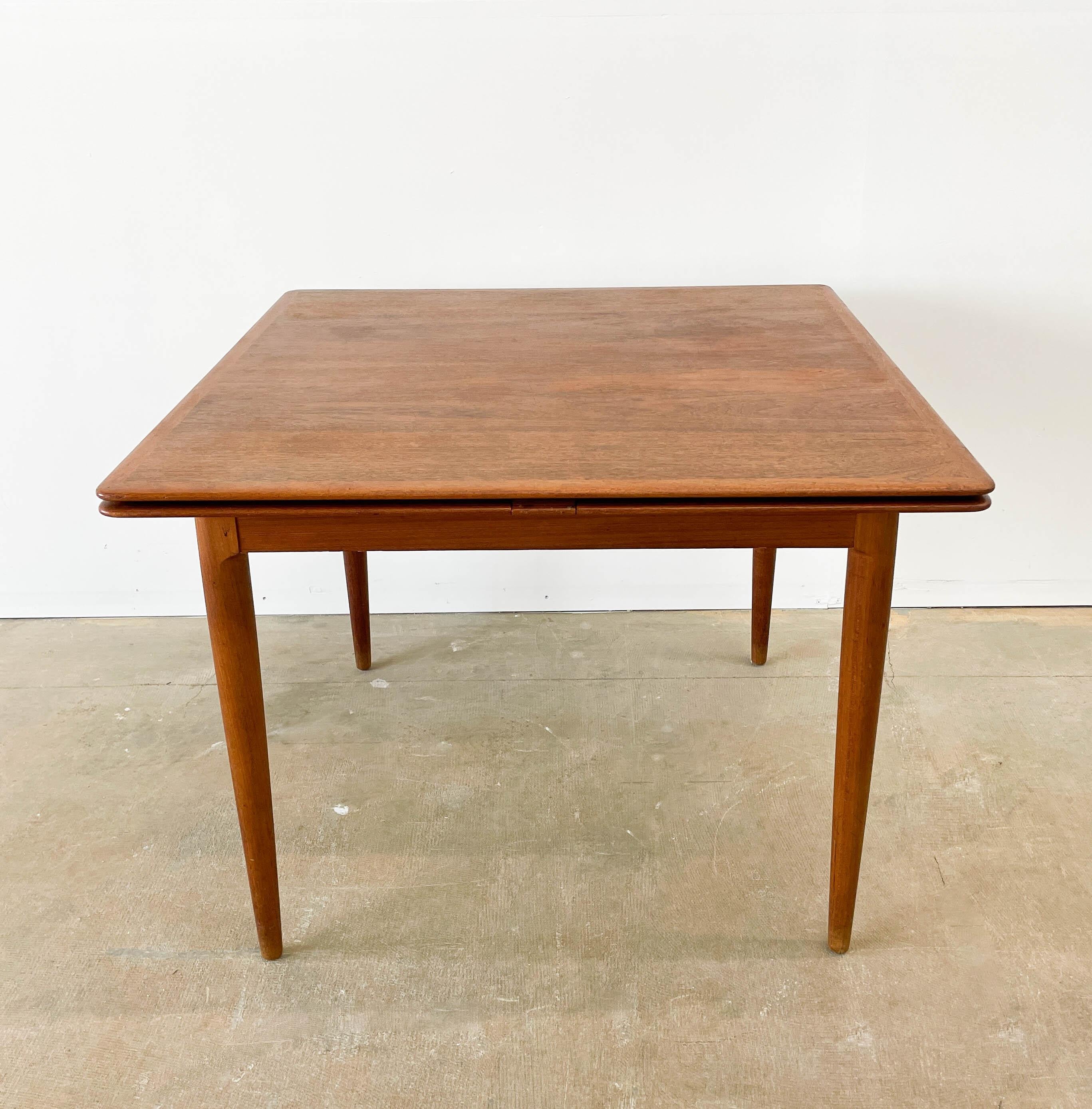 Imported by Morreddi in the 1960s, this Danish Mid-Century Modern teak table expands from a square shape to a larger rectangle. When fully expanded, the table can seat 6-8 people. The pull-out leaves boast recessed handles, and the leaves are stored