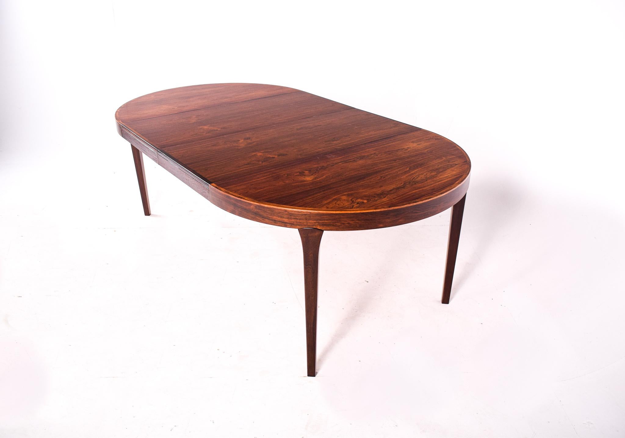 Round dining table, veneered with rosewood. Tapered legs, top with two extension leaves with apron, each 49 cm. This exceptional dining table features beautiful proportions, the weight of the round table top is balanced by the lightness of the
