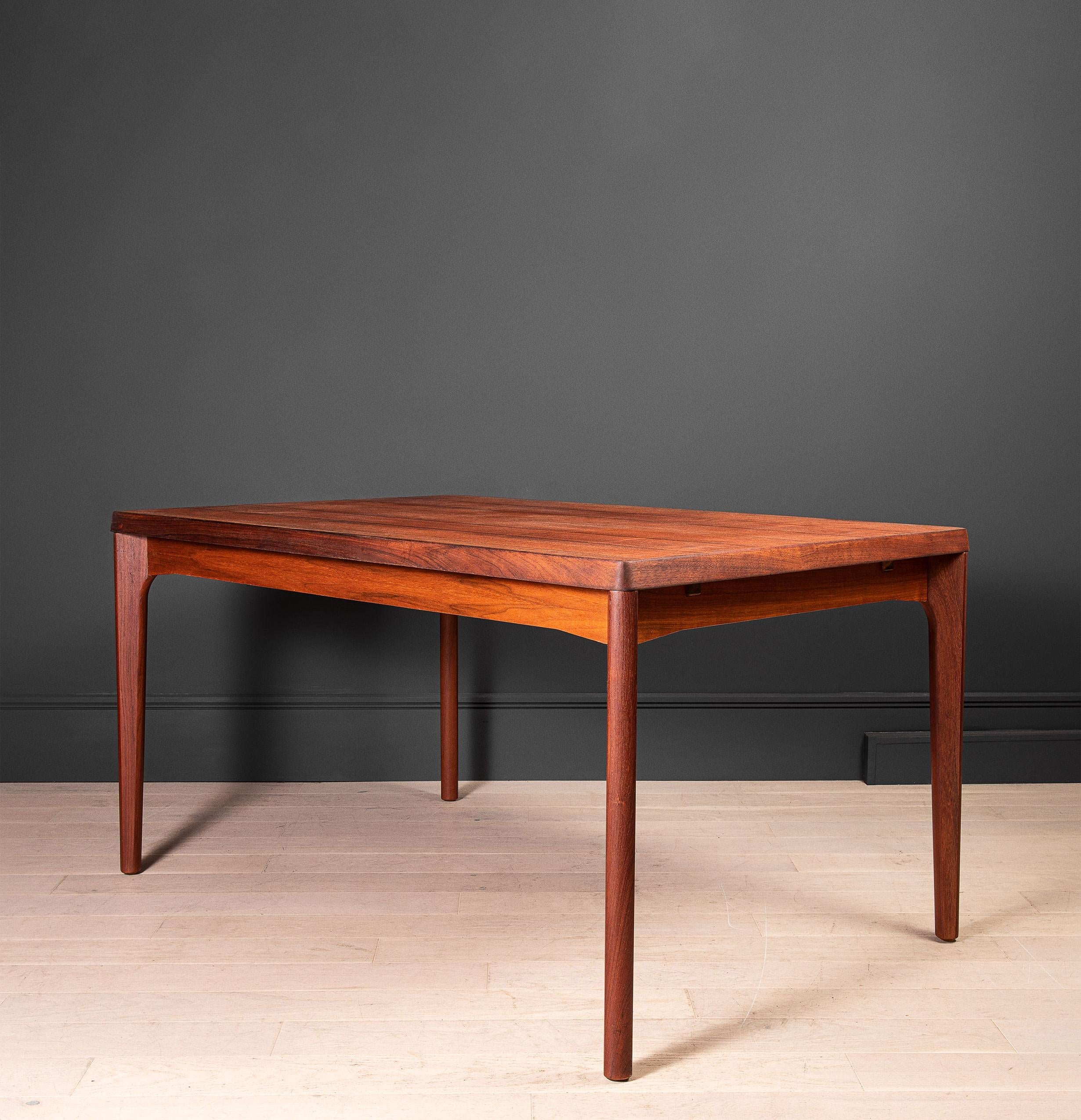 Une jolie table minimaliste conçue par Henning Kjaernulf. Fabriqué en teck, il est doté de deux panneaux coulissants cachés sous la surface principale. Danemark vers 1960. Le jeu de 8 chaises Henning est également disponible séparément.