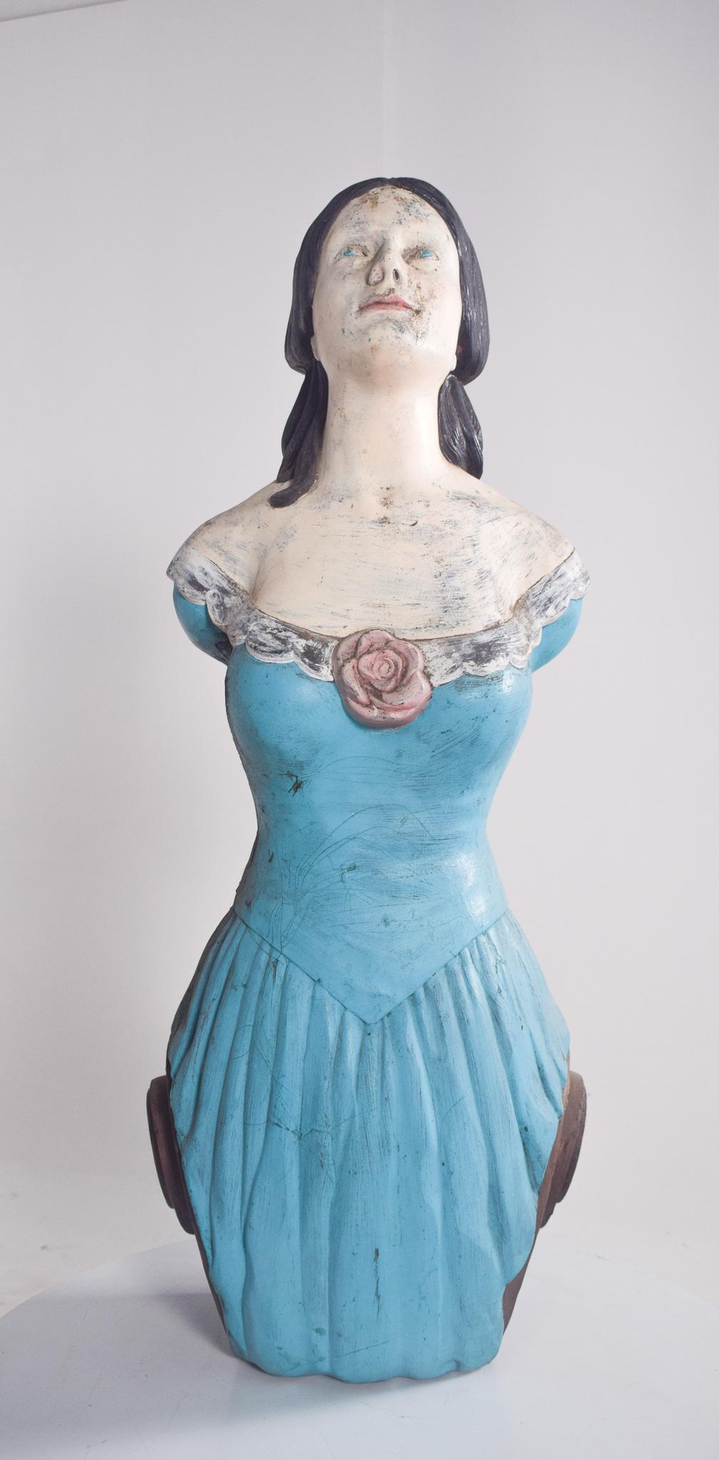 Figura femminile, scultura in fibra di vetro. Con i suoi lineamenti classici e lo sguardo leggermente rivolto verso l'alto, indossa un abito blu off-the-shoulder con dettagli sul bordo e una rosa centrale sulla scollatura. I suoi capelli scuri, che