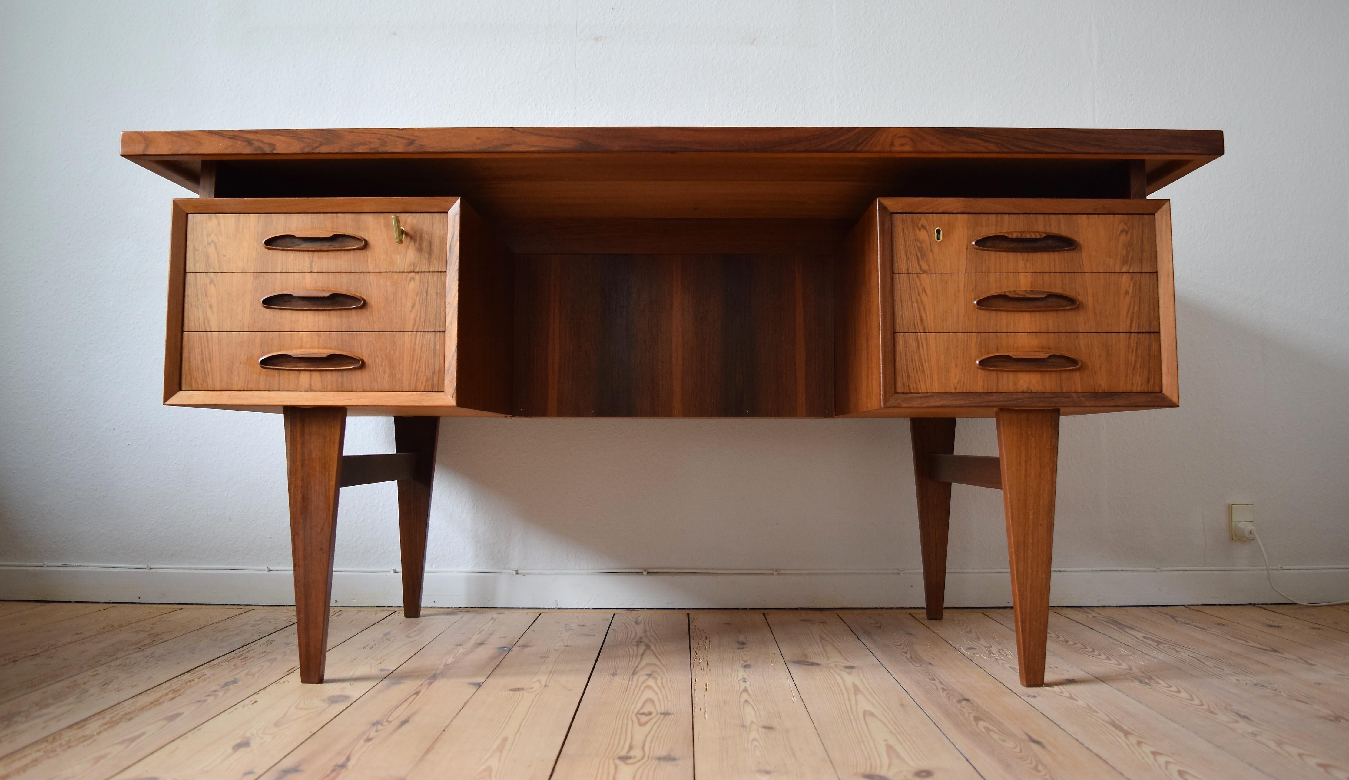Rosewood floating desk manufactured in Denmark in the 1960s. This freestanding desk features a floating top with six drawers on the front, two lockable(keys included). Three bookcase sections on the rear with bevelled edges. The construction