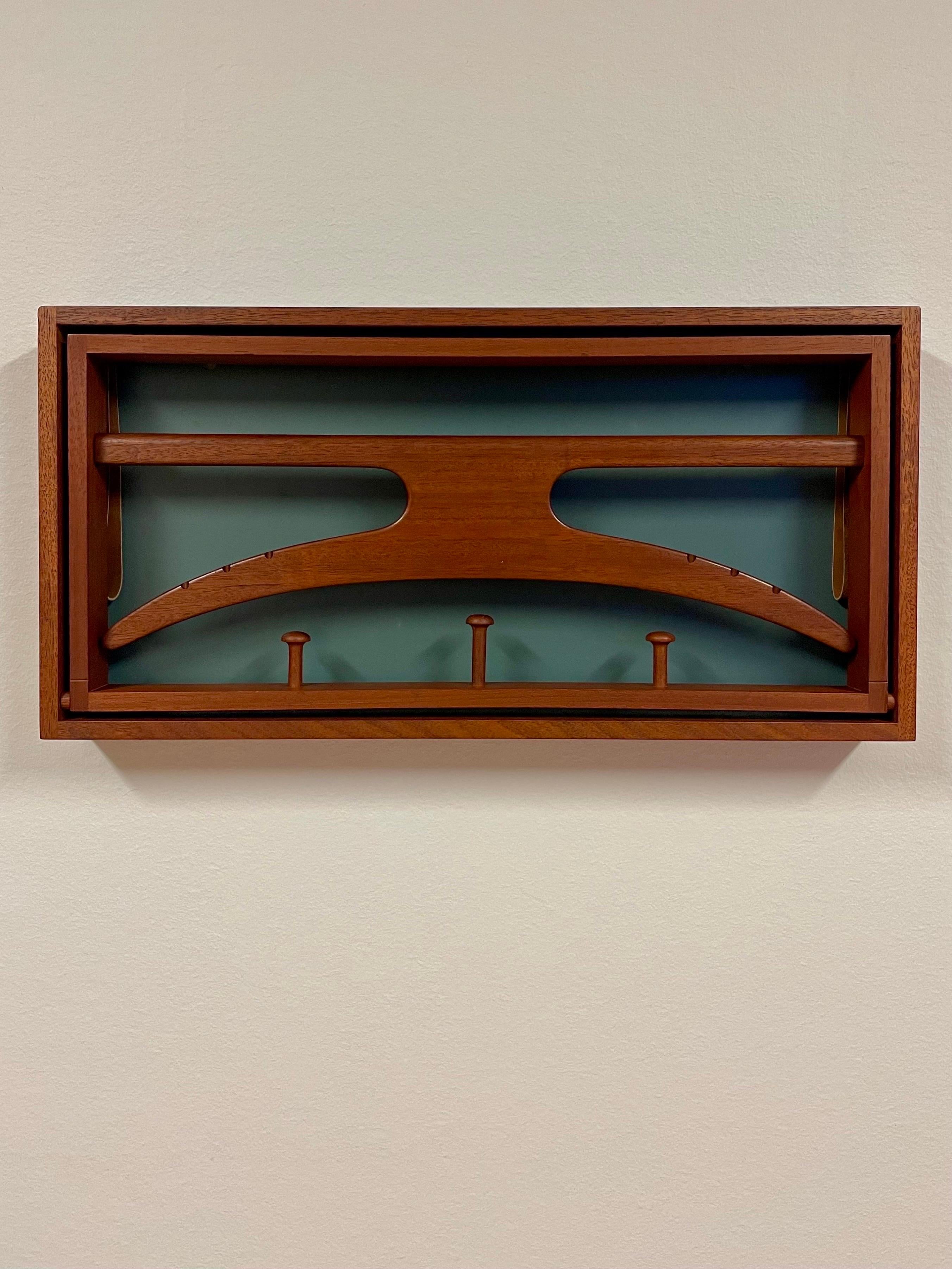 This is the 1960s foldable valet by Adam Hoff & Poul Østergaard for Virum Møbelsnedkeri, mainly retailed by Illums Boglighus. 
It comes in a construction intended for wall mounting. 

The lacquered back is made of masonite. Frames, coat hanger and