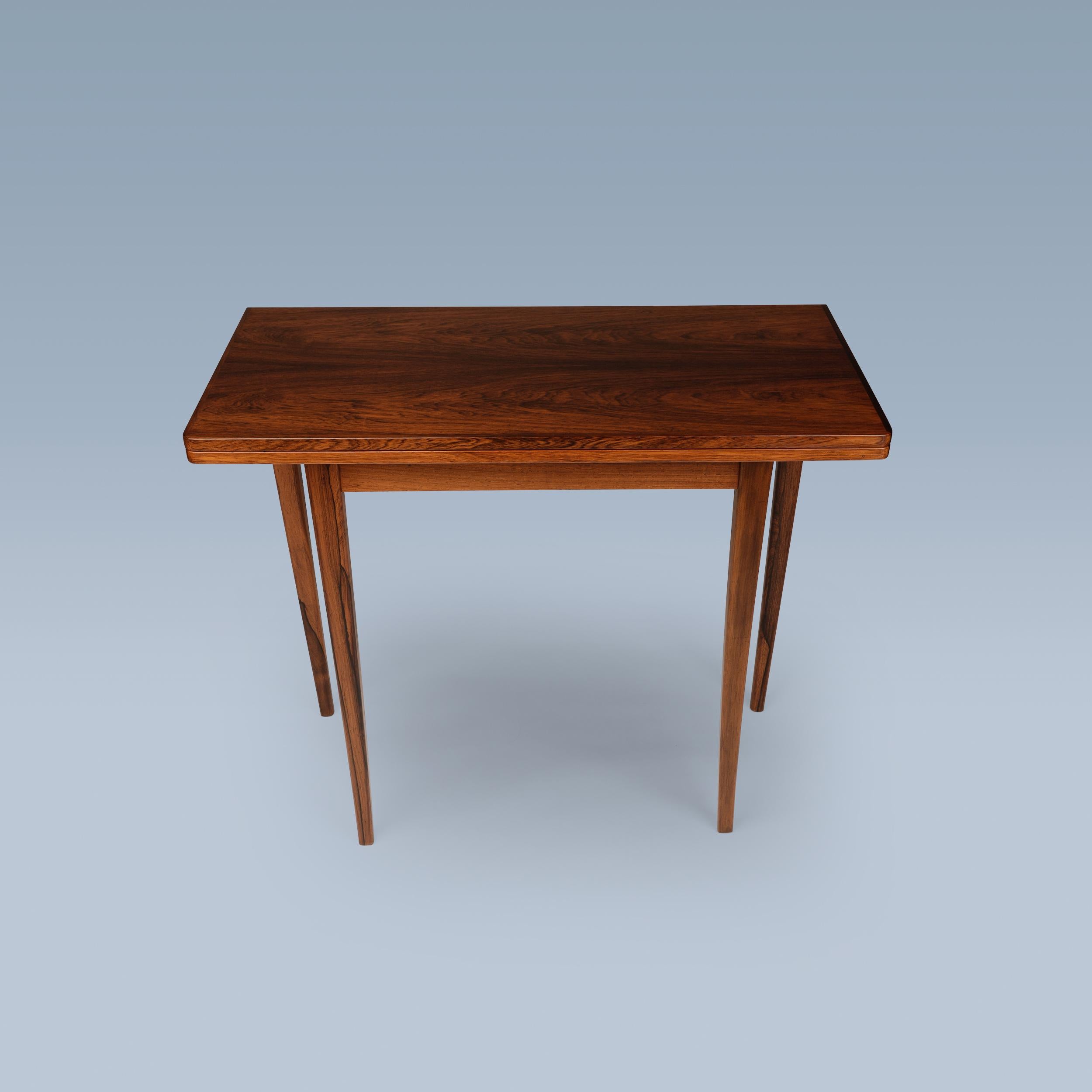 Dieser elegante Spiel- und Kartentisch aus Palisanderholz lässt sich auf die halbe/doppelte Größe falten. Er hat eine Tischplatte mit dekorativen blau getönten Fliesen in den Ecken und Messingbeschlägen.

Der Tisch wurde ca. in den 1950-1960er