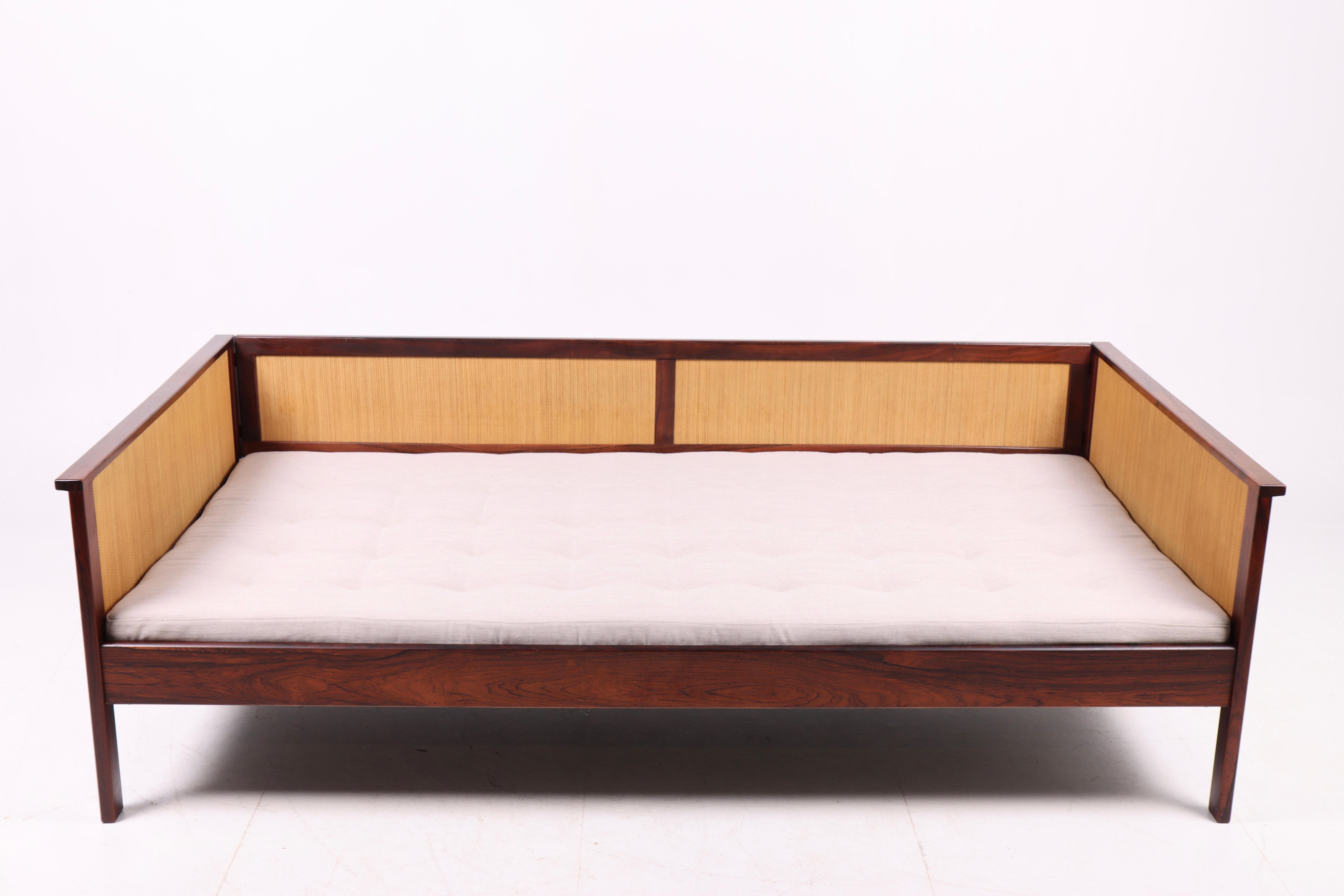 Elegante divano-letto indipendente prodotto in Danimarca negli anni Sessanta. La struttura è realizzata in legno di palissandro con venature meravigliose e i lati sono dotati di pannelli di canna che conferiscono al pezzo un'espressione leggera ed