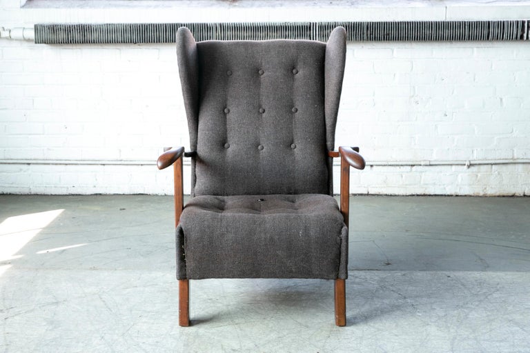 Very cool low swung wingback lounge chair made by Fritz Hansen in Copenhagen, Denmark. Great dramatic angles and proportions with carved wooden armrests and legs made of stained beech wood showing great grain and patina and just minor natural wear.