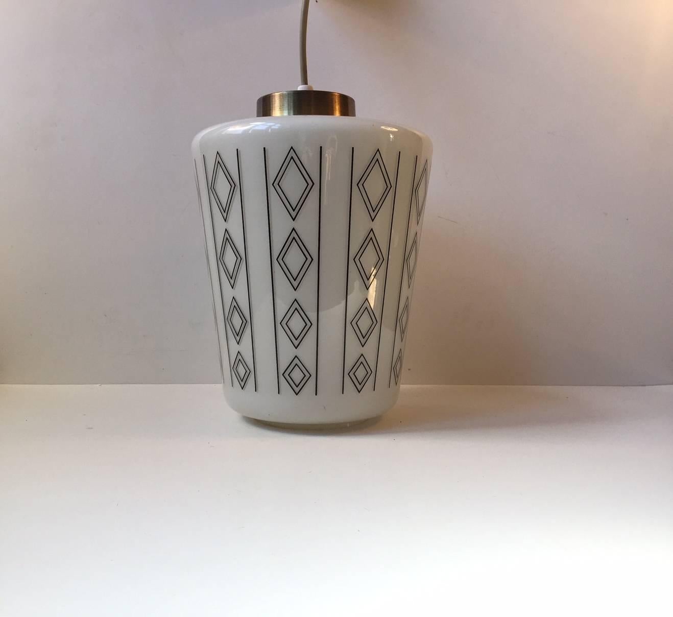 This Danish pendant light features a white opaline glass diffuser set in brass. It is decorated around its perimeter with black geometric decor. It was manufactured and designed in Denmark during the 1950s in a style reminiscent of Lyfa and Fog &