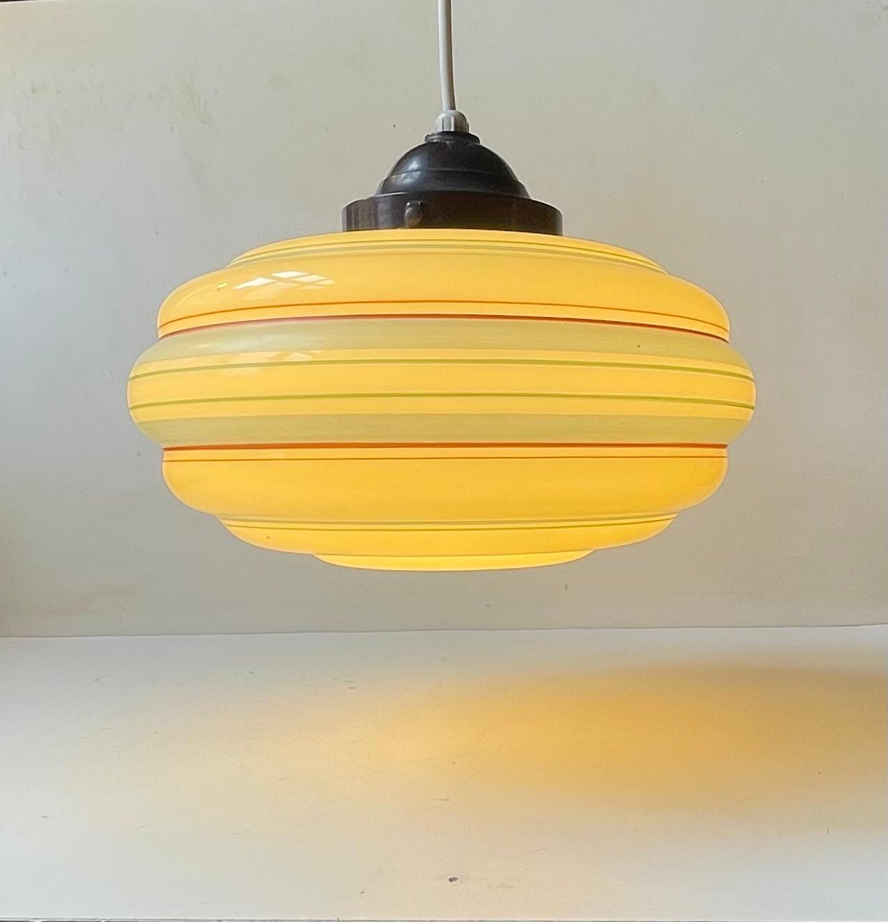 A beehive shaped ceiling lamp composed of pastel yellow toned opaline glass shade decorated with blue, green, red and orange horizontal stripes. It still retains its original bakelit socket/top. It was made in Denmark during the 1930s in a style