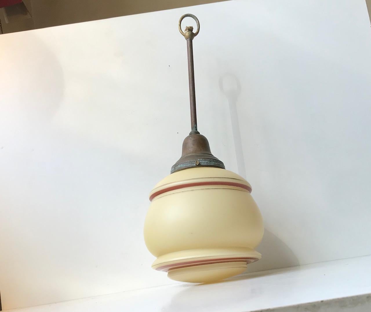 Lampada a sospensione per ingresso composta da vetro opalino giallo pastello decorato a strisce. Il pendente è caratterizzato da una presa in ottone patinato a forma di tronco. È stata prodotta in Danimarca negli anni '30 o '40.