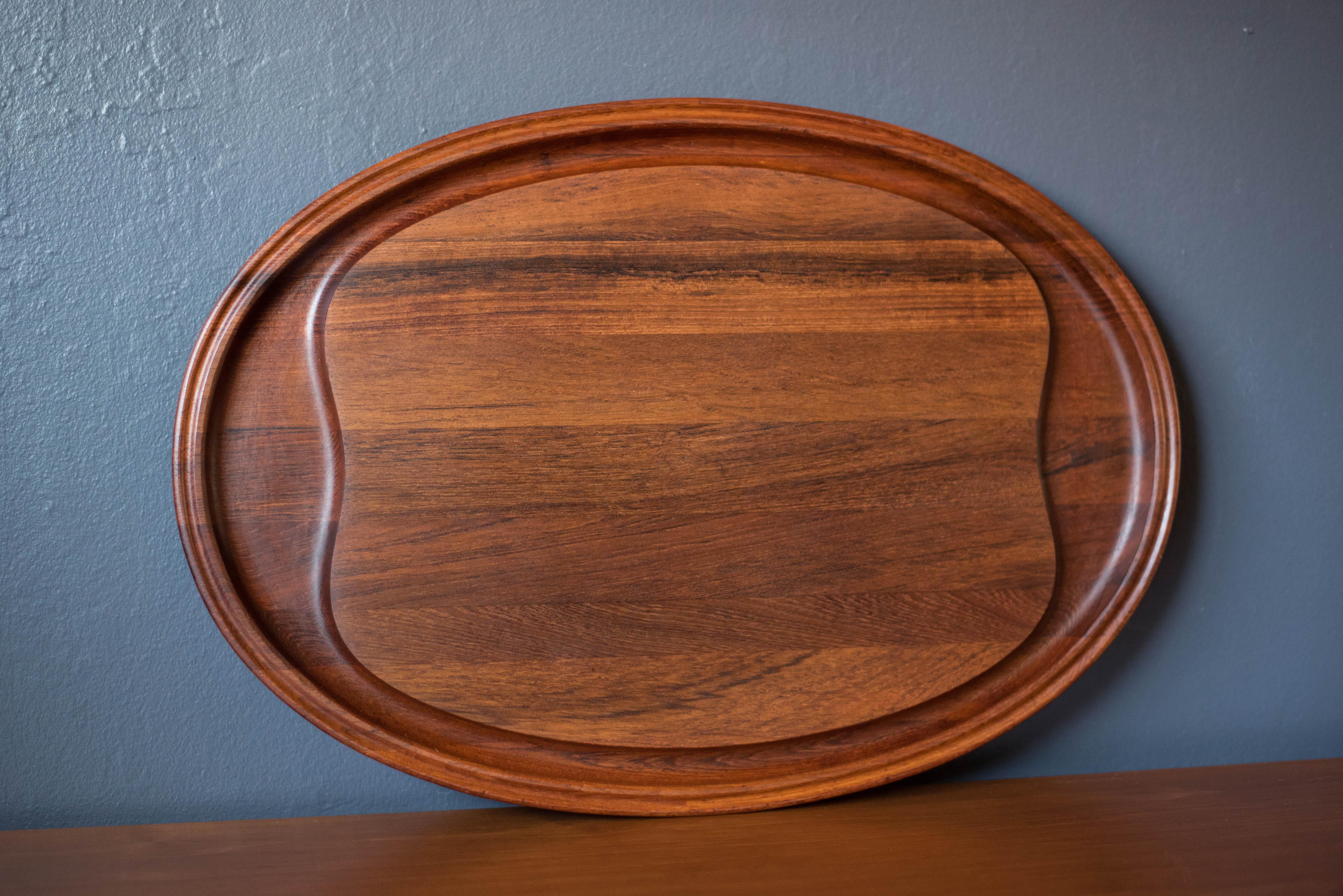 Mid-Century Modern cutting board platter designed by Henning Koppel for Georg Jensen, Denmark. This sculptural oval tray displays rich solid teak grains with deep grooves intended for both prepping and serving. Perfect to accessorize as a display