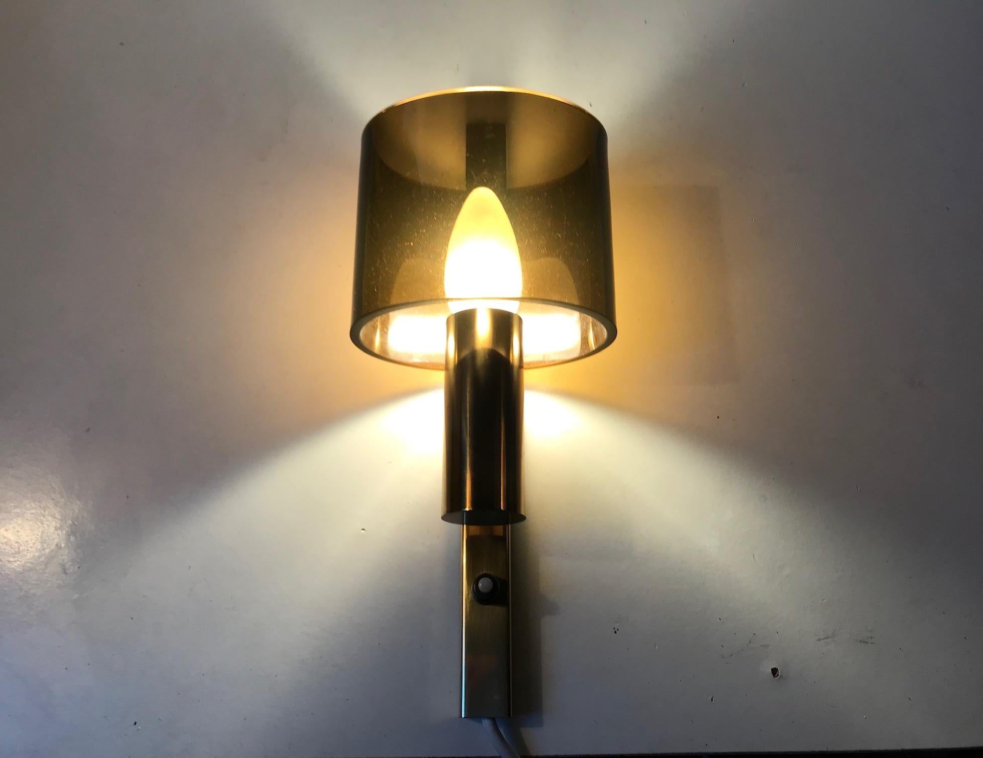 Un aplique raro y elegante compuesto de latón dorado que sostiene una pantalla ovalada de Lucite ahumado. Diseñada y fabricada por Hassel & Teudt en Dinamarca a mediados y finales de la década de 1960.